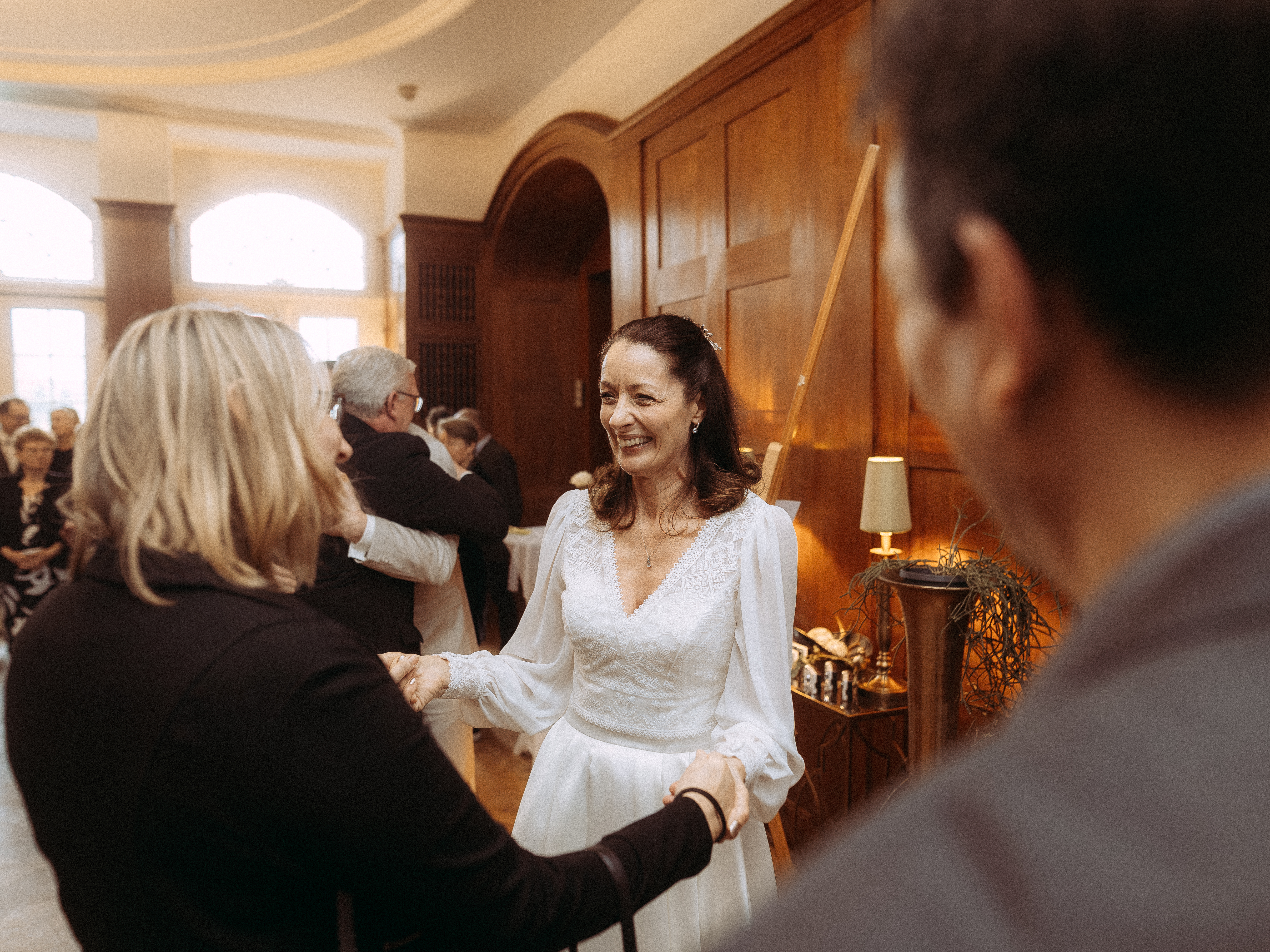 Lächelnde Braut im weißen Kleid wird auf einer Hochzeitsfeier begrüßt.