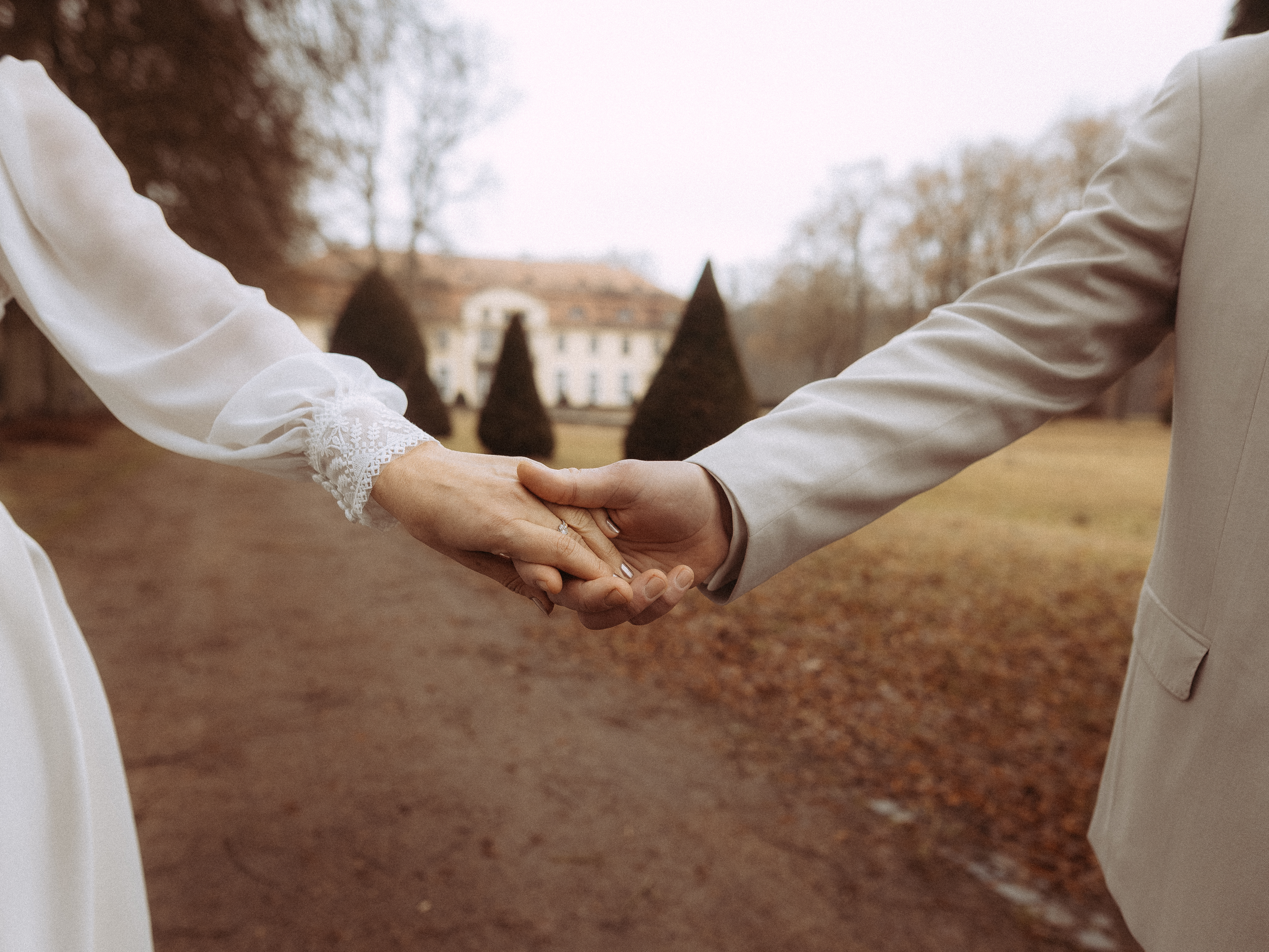 Brautpaar hält Hände mit Ehering vor Schloss. Hochzeit im Park.