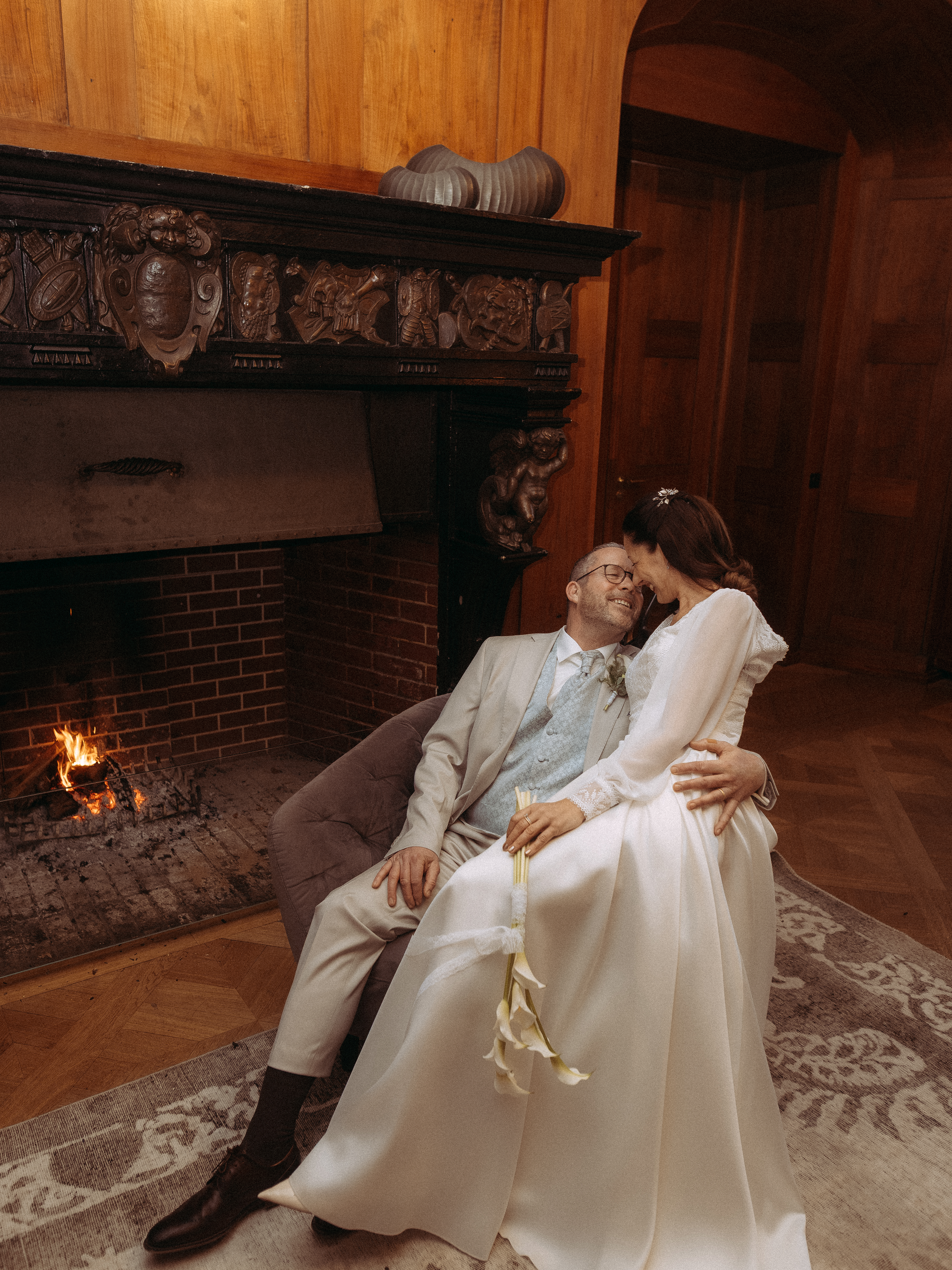 Brautpaar kuschelt am Kamin in historischem Ambiente. Hochzeit, Liebe, Wärme.