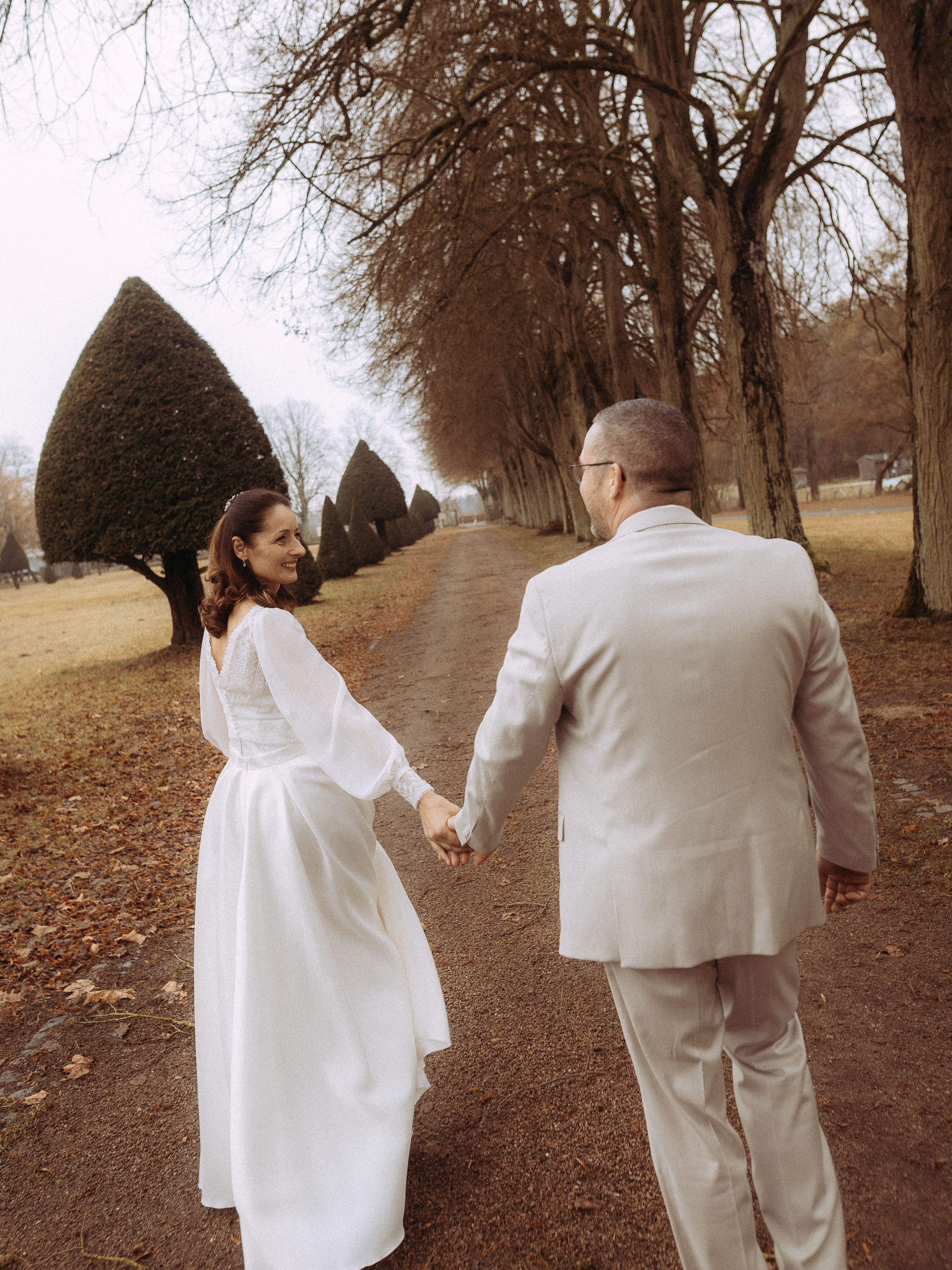 Brautpaar Hand in Hand auf einem Weg mit Bäumen. Hochzeit im Herbst.