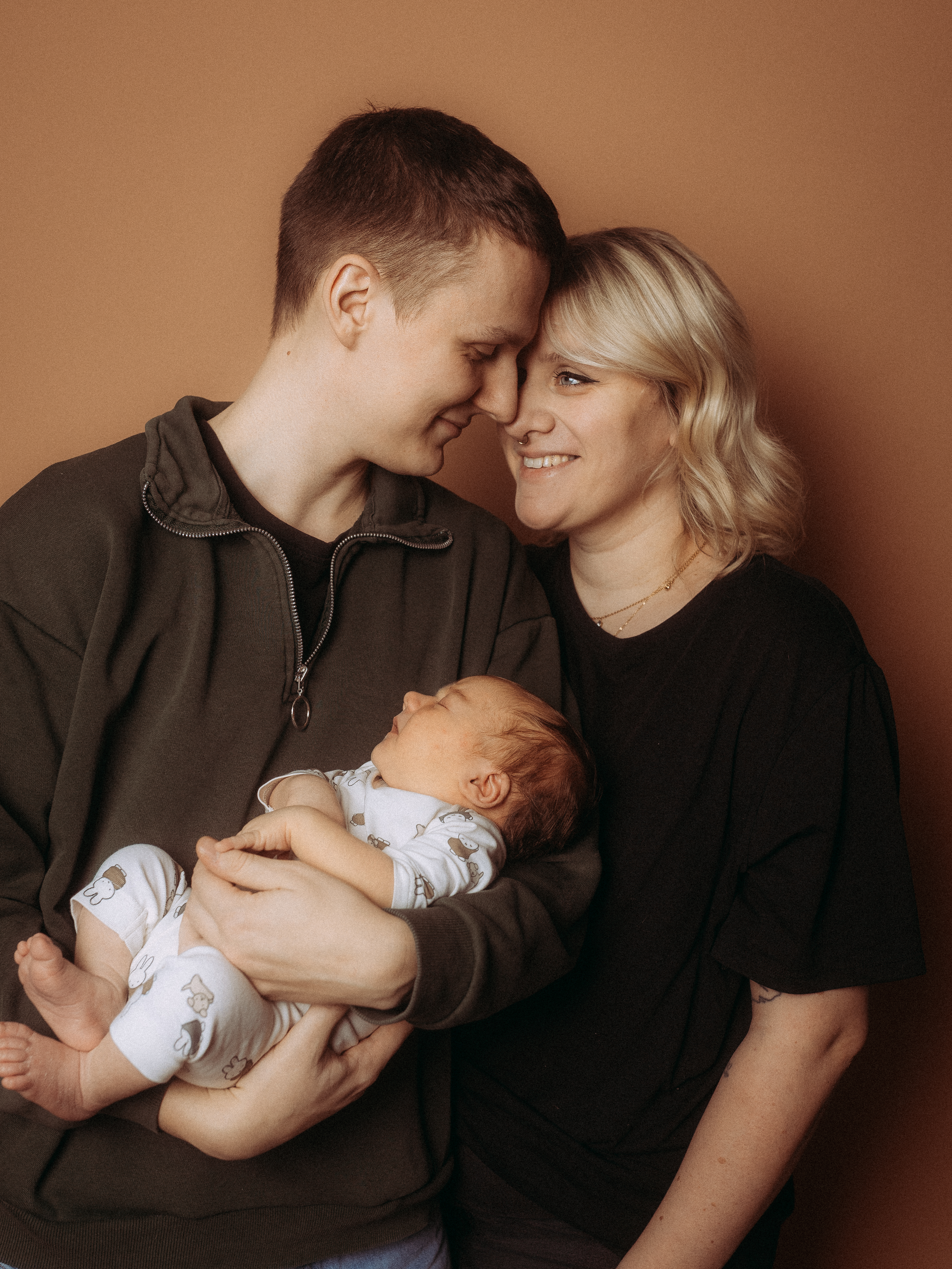 Glückliche Eltern halten ihr Neugeborenes im Arm, lächelnd und liebevoll.