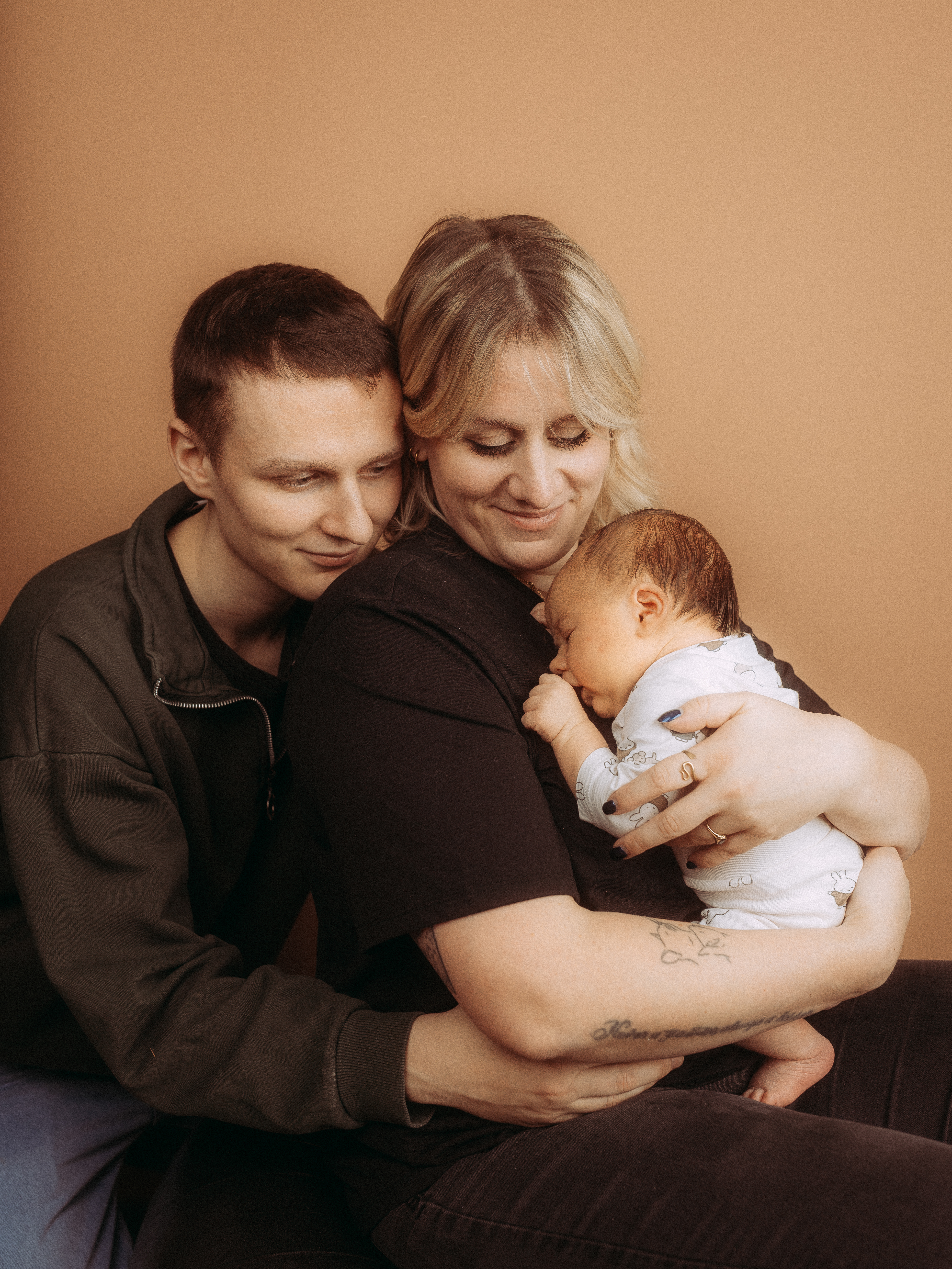 Glückliche junge Familie: Mutter hält Neugeborenes im Arm, Vater schaut liebevoll zu.