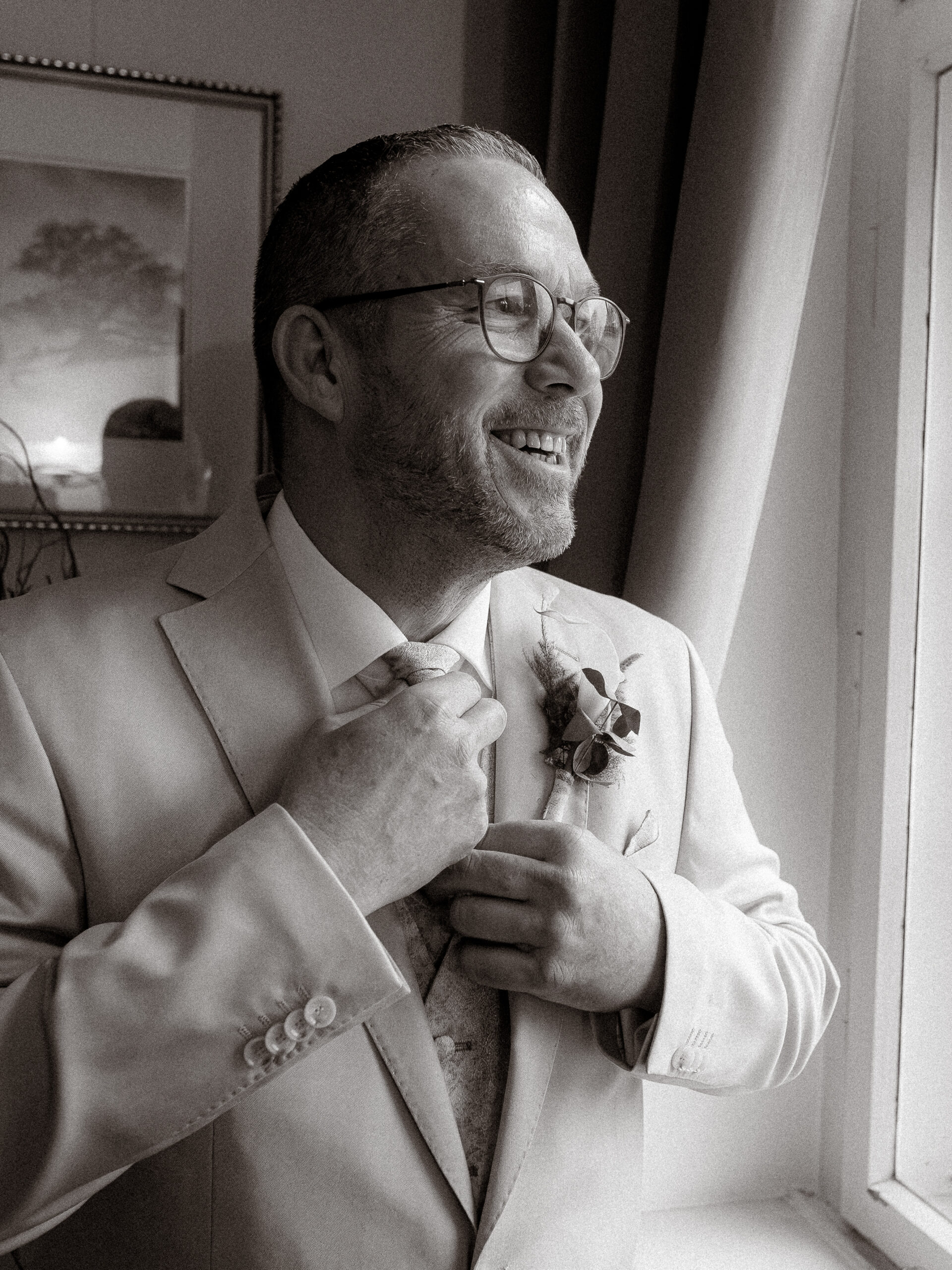 Bräutigam im Anzug bindet Krawatte, lächelt am Fenster. Hochzeitstag Vorfreude.