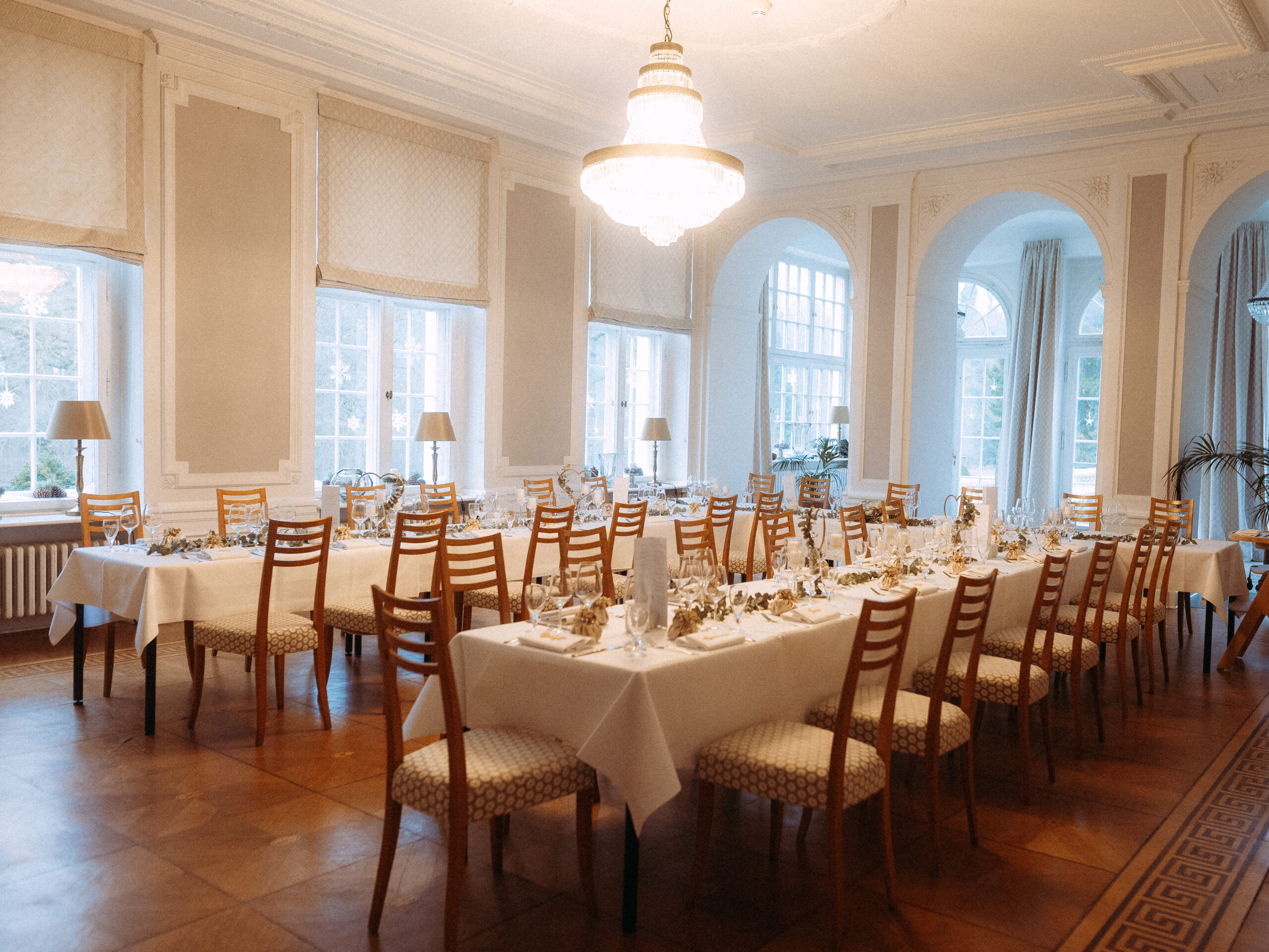 Festlich gedeckte Hochzeitstafel in einem eleganten Saal mit Kronleuchter und großen Fenstern.