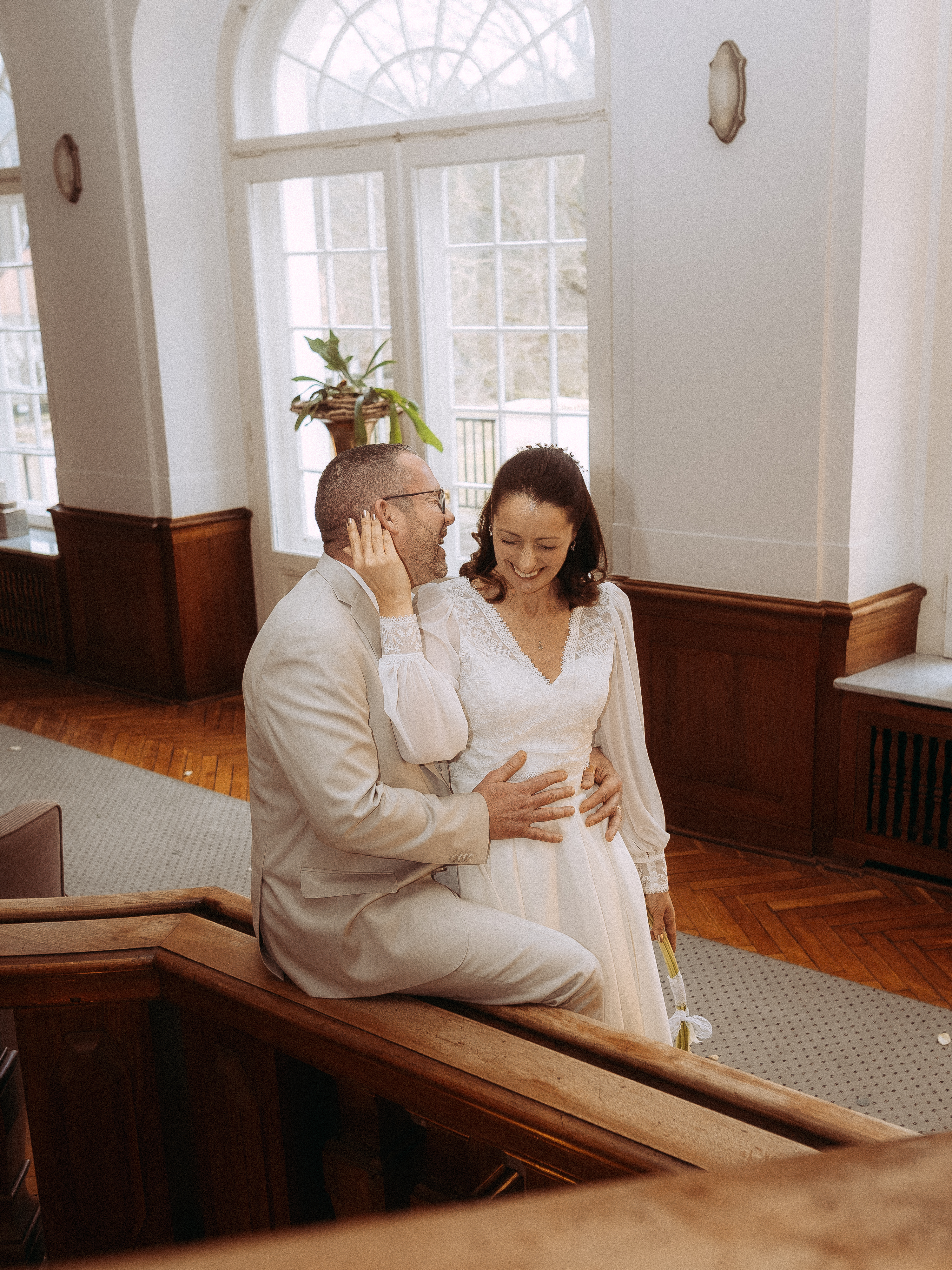 Glückliches Hochzeitspaar in heller Halle mit Holzvertäfelung. Braut und Bräutigam lachen.