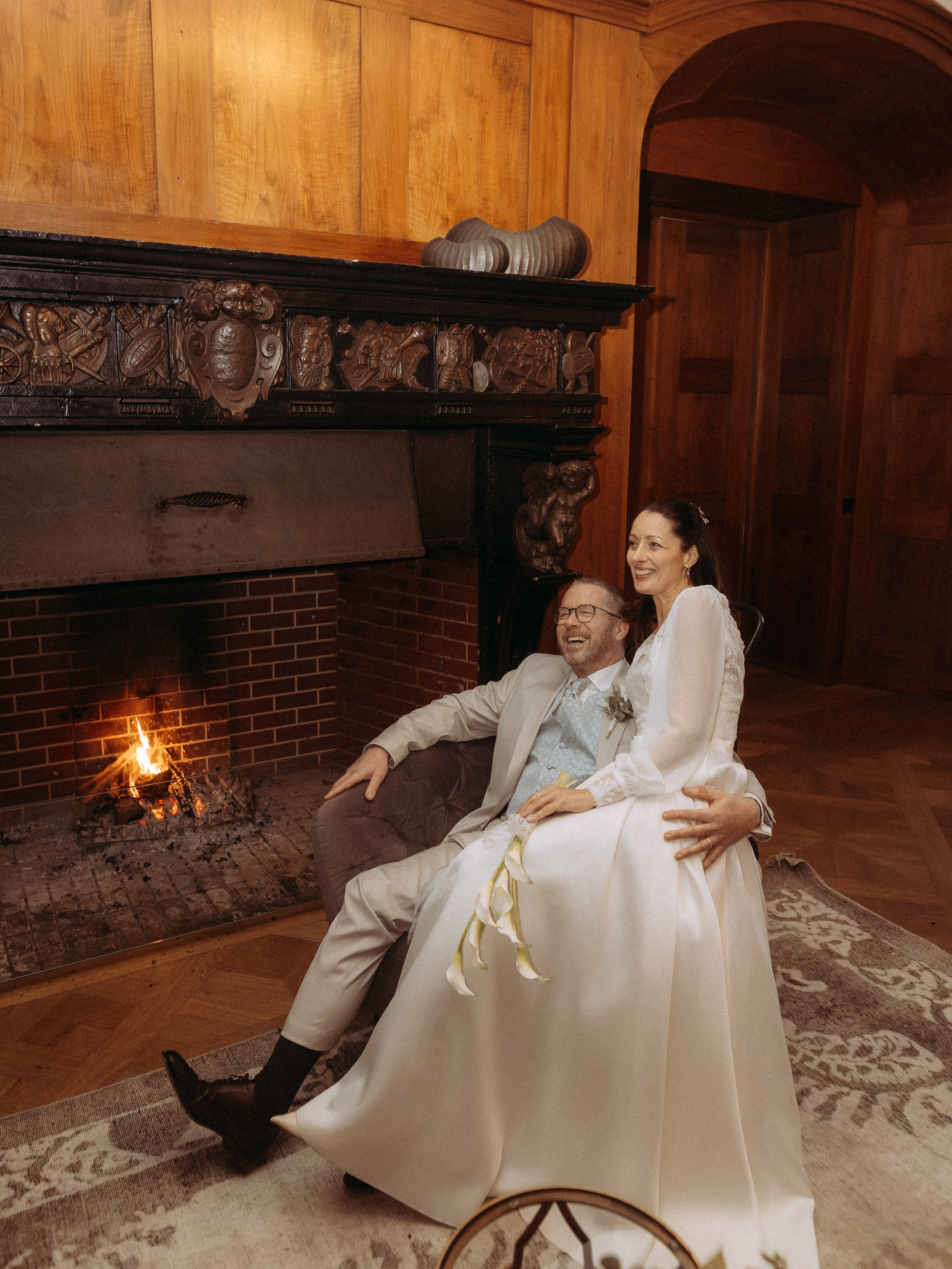 Glückliches Brautpaar kuschelt am Kamin in festlicher Hochzeitslocation.