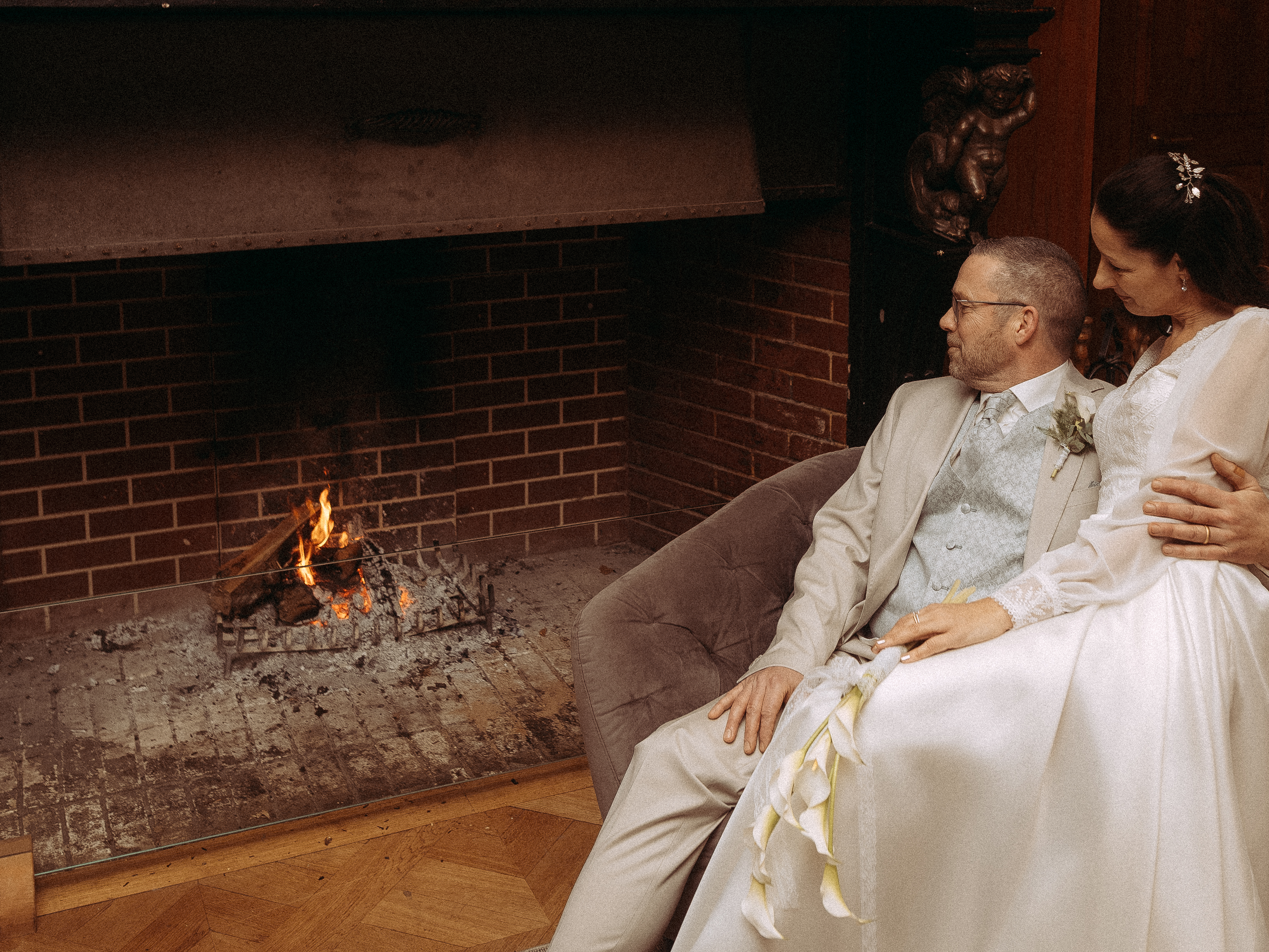 Brautpaar kuschelt am Kaminfeuer, Braut hält Calla Lilien