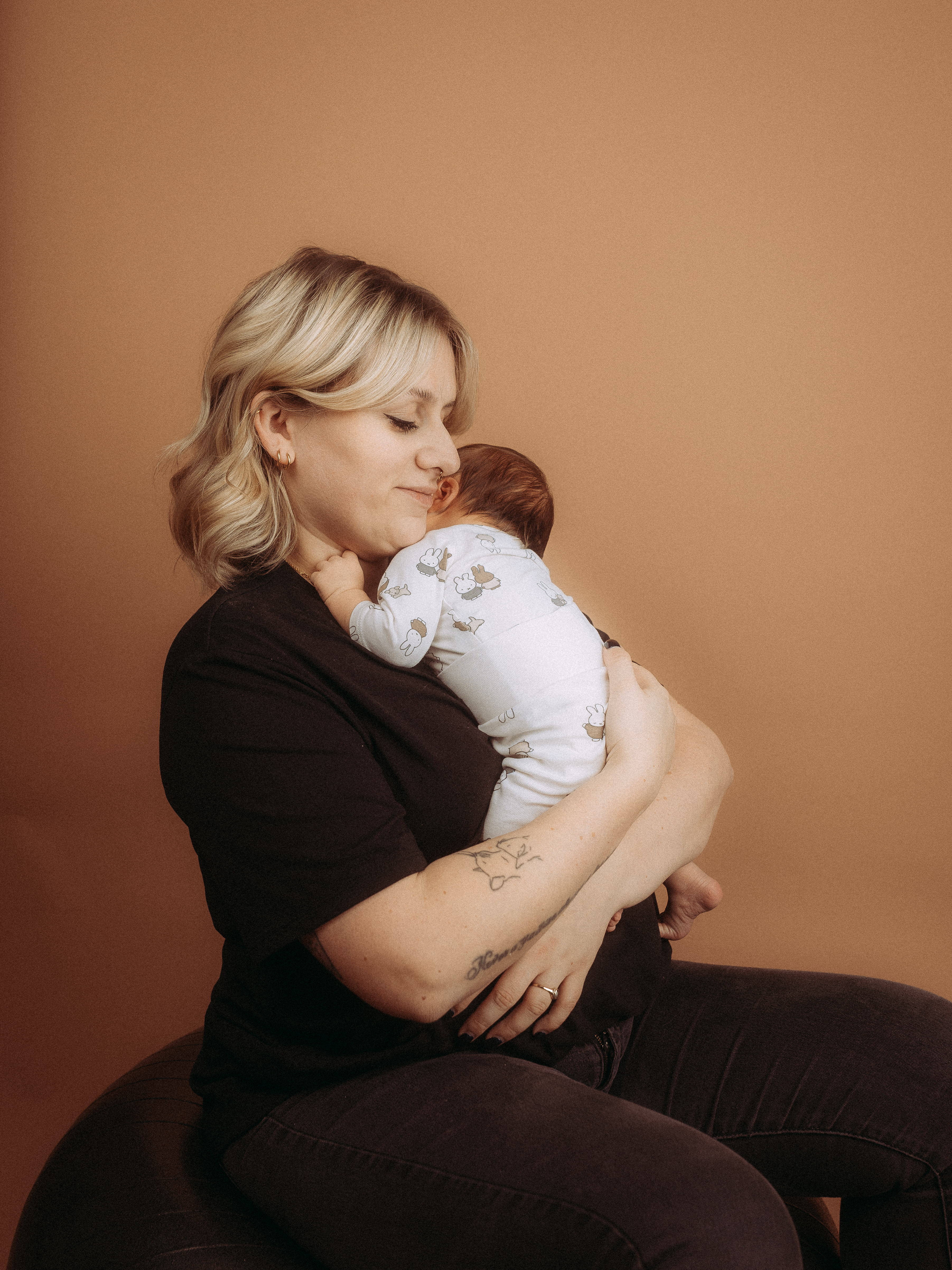 Mutter hält liebevoll ihr Baby im Arm, sanftes Braun im Hintergrund