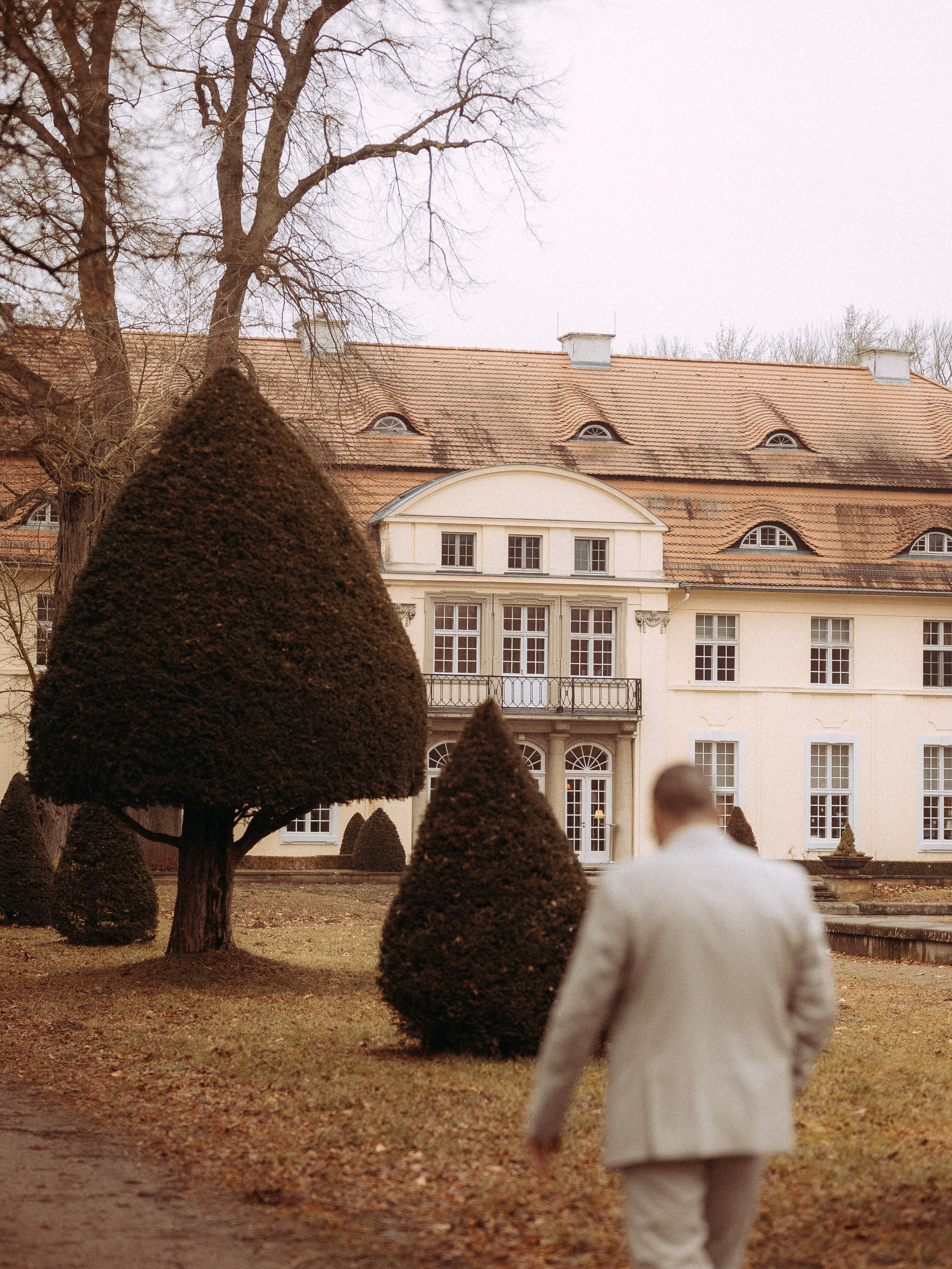 Mann geht auf ein elegantes Schloss zu, umgeben von gepflegten Gärten.
