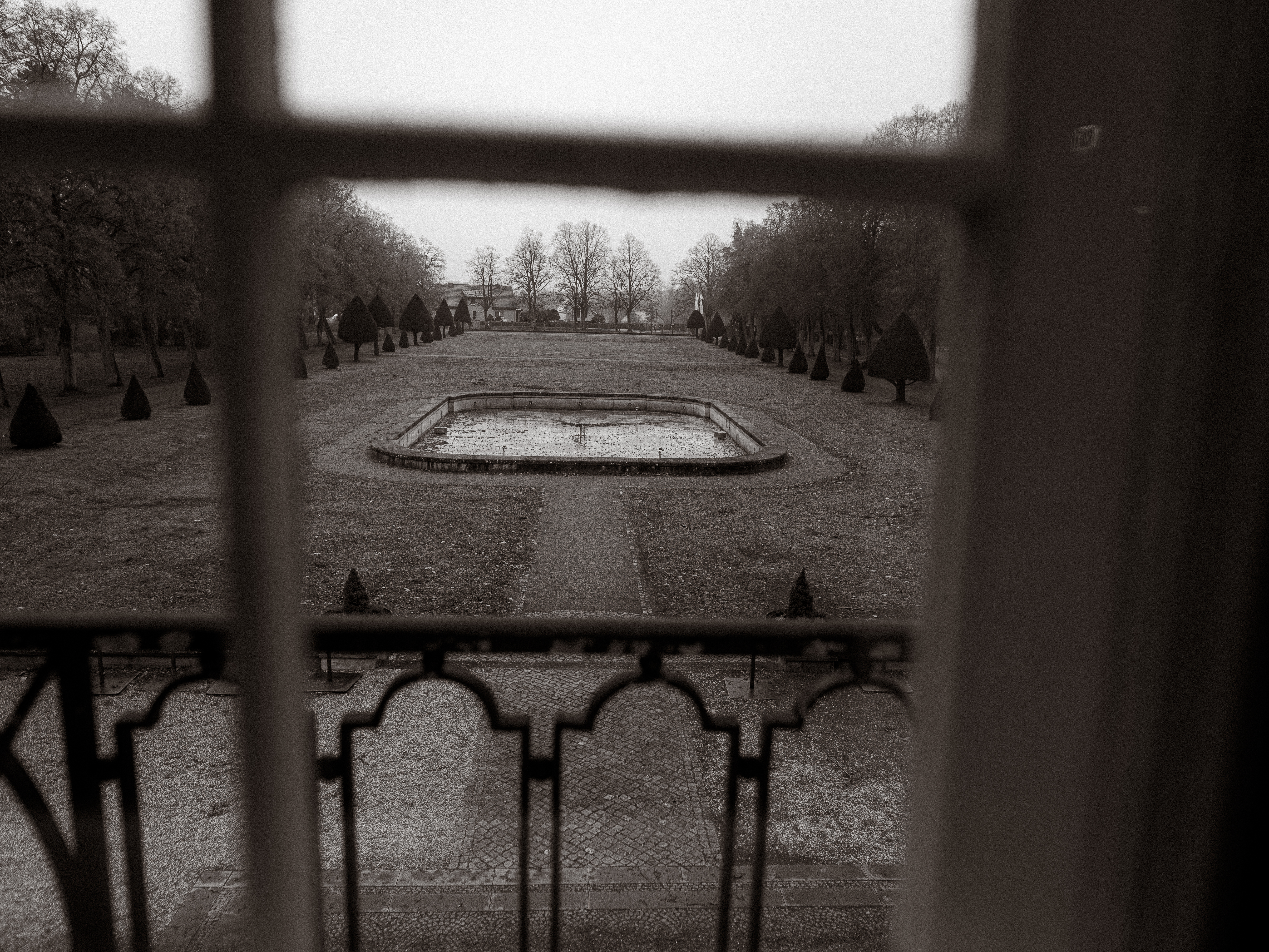 Formaler Garten mit einem zentralen rechteckigen Teich, der im Winter von kahlen Bäumen umgeben ist.