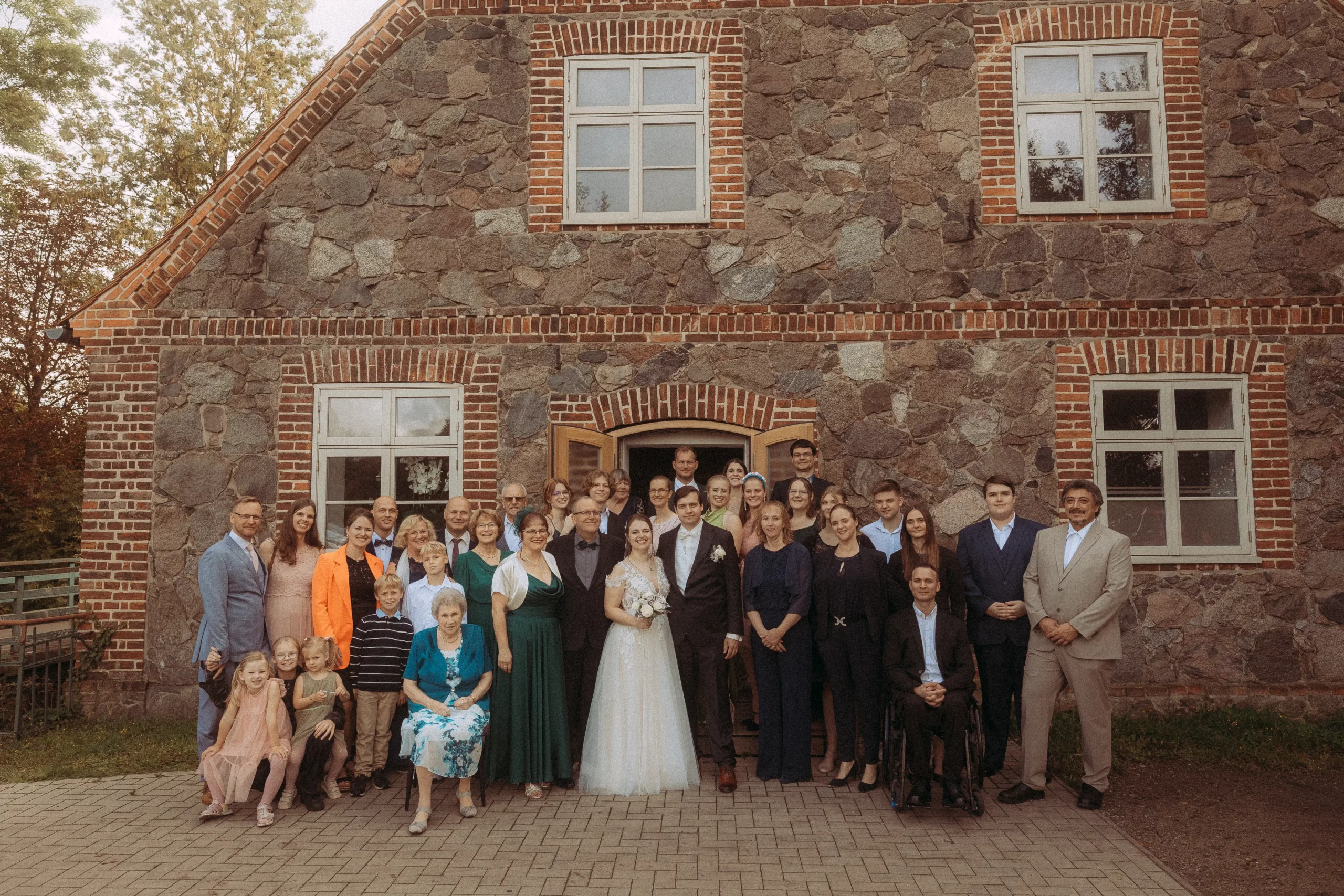 Hochzeitsfotograf vor Backsteingebäude mit Hochzeitsgesellschaft