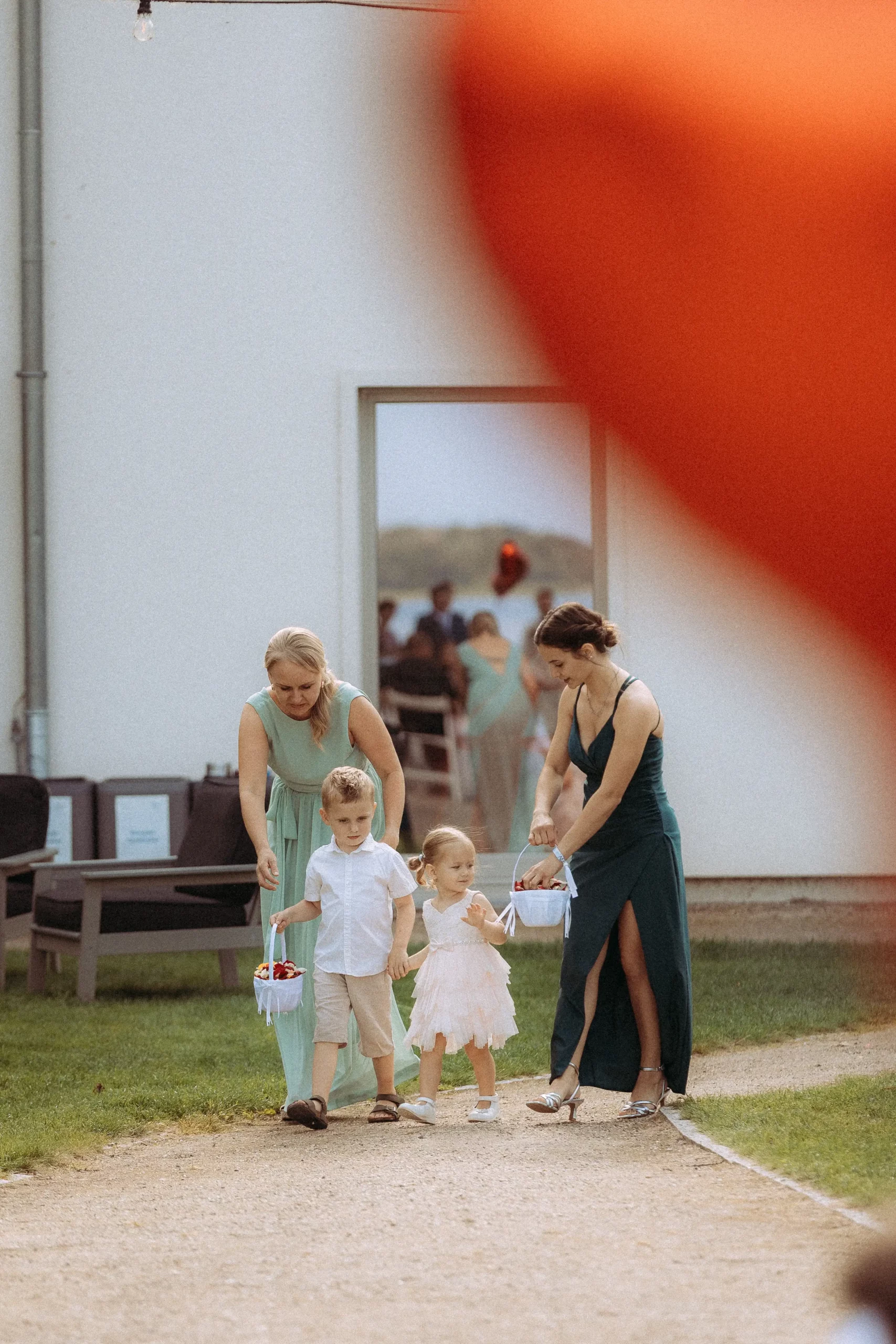 Zwei Frauen in blaugrünen Kleidern gehen auf einem Gartenweg, jede hält die Hand eines kleinen Kindes in Weiß. Die Gruppe bewegt sich auf die Kamera zu, mit einem roten Fleck teilweise rechts - aufgenommen von einem Fotografen in Schwerin.
