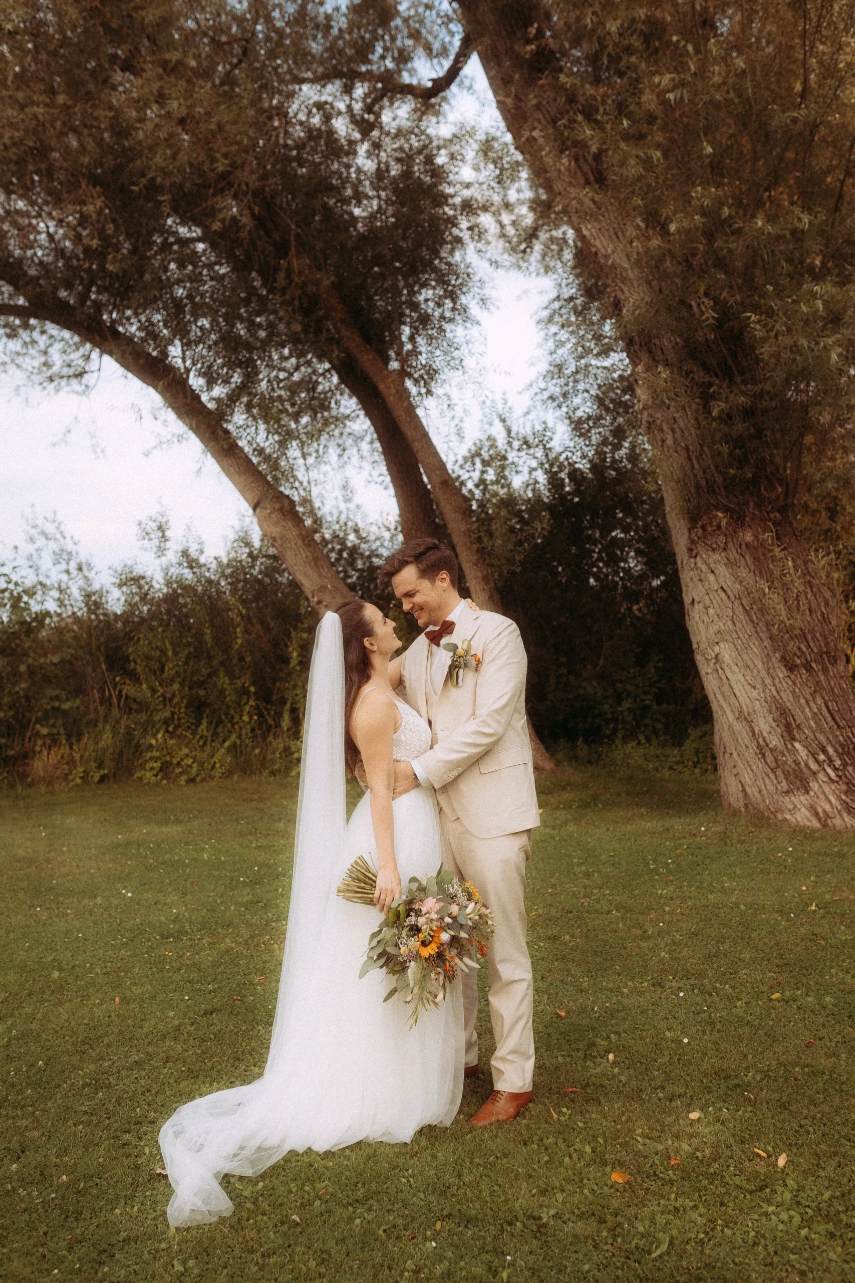 Brautpaar umarmt sich unter Baum