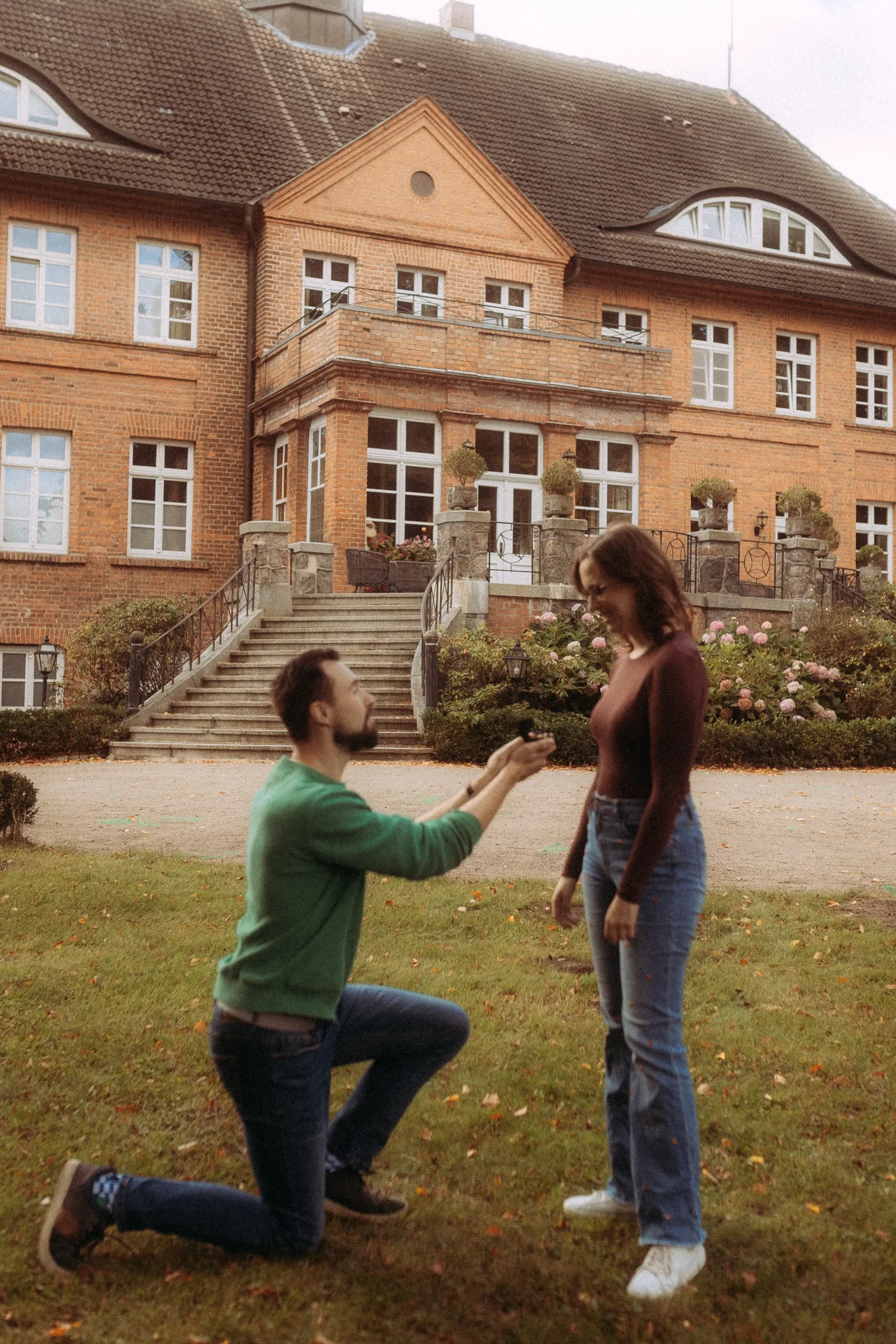 Mann macht Heiratsantrag vor einem Herrenhaus.