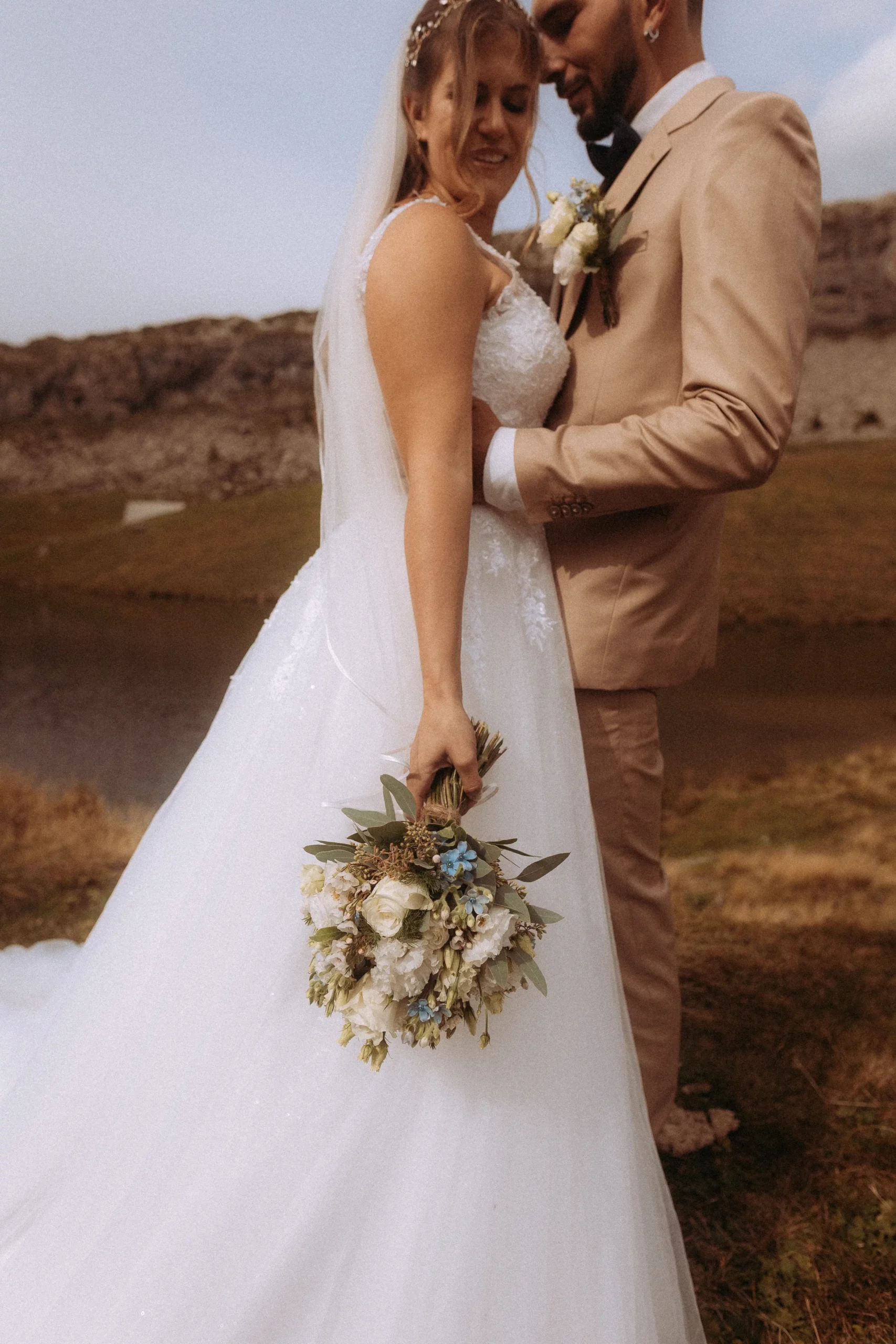 Brautpaar in den Bergen, sie hält einen Blumenstrauß. Der Hochzeitsfotograf in MV hat die intime Szene eingefangen, mit Blick auf einen kleinen See. Die Hochzeit wirkt natürlich und liebevoll.