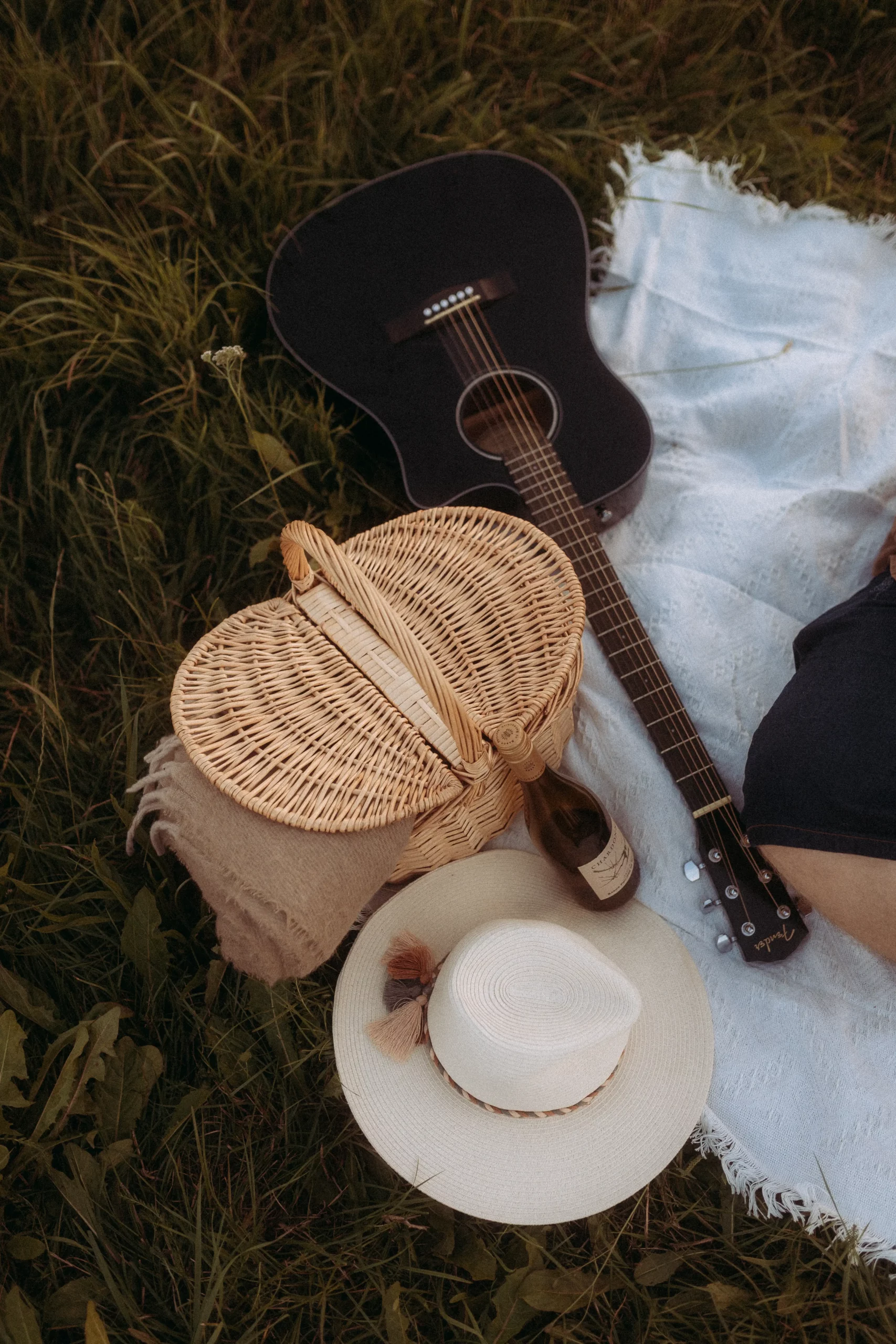 Picnic basket, guitar, and blanket on grass.