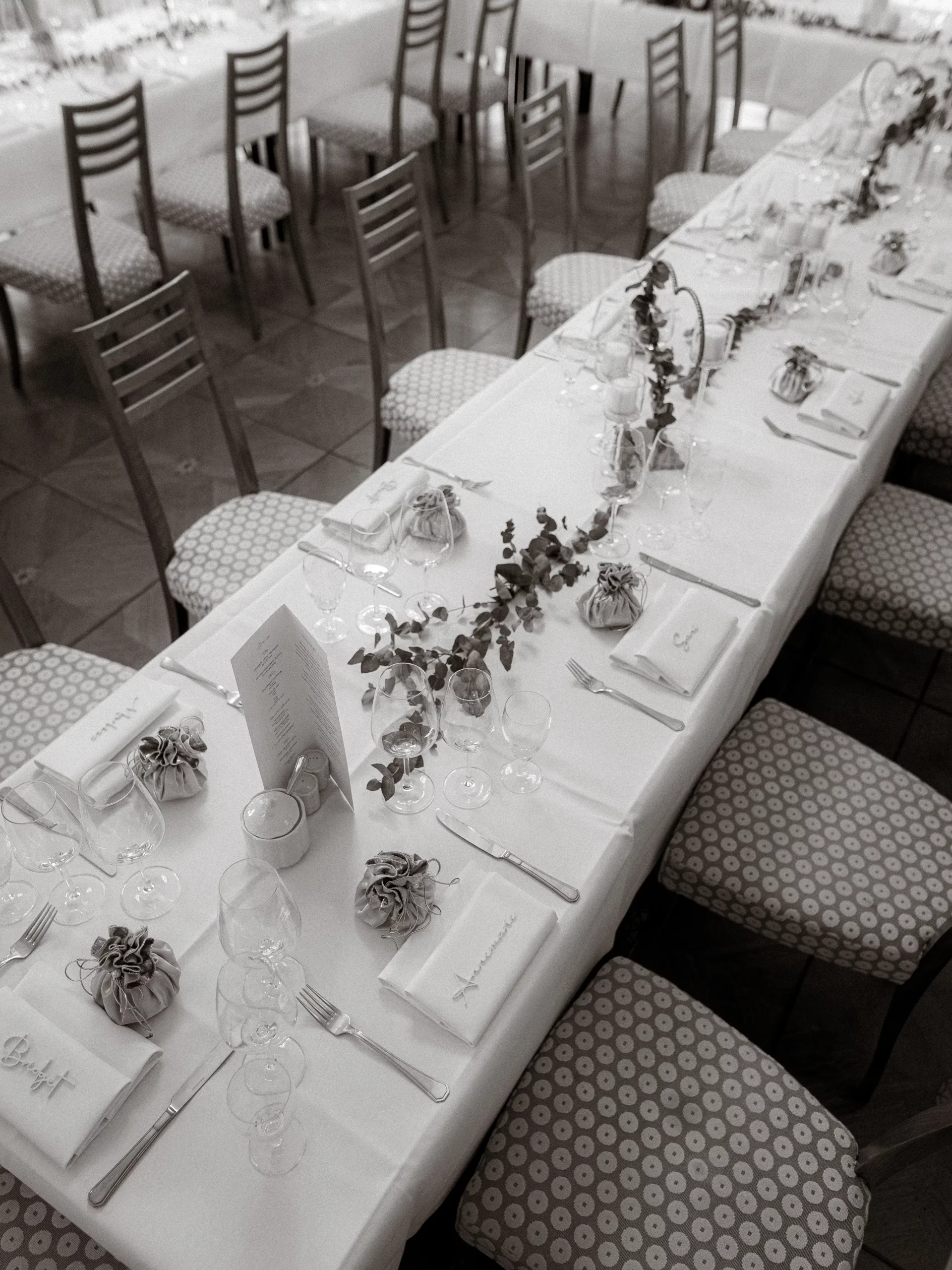 Ein langer, elegant gedeckter Tisch mit weißem Tischtuch, Gläsern, Speisekarten, Servietten und kleinem Blumenschmuck erwartet die Gäste bei einer feierlichen Veranstaltung - perfekt für Hochzeitsfotos MV von einem Hochzeitsfotograf aus Schwerin.