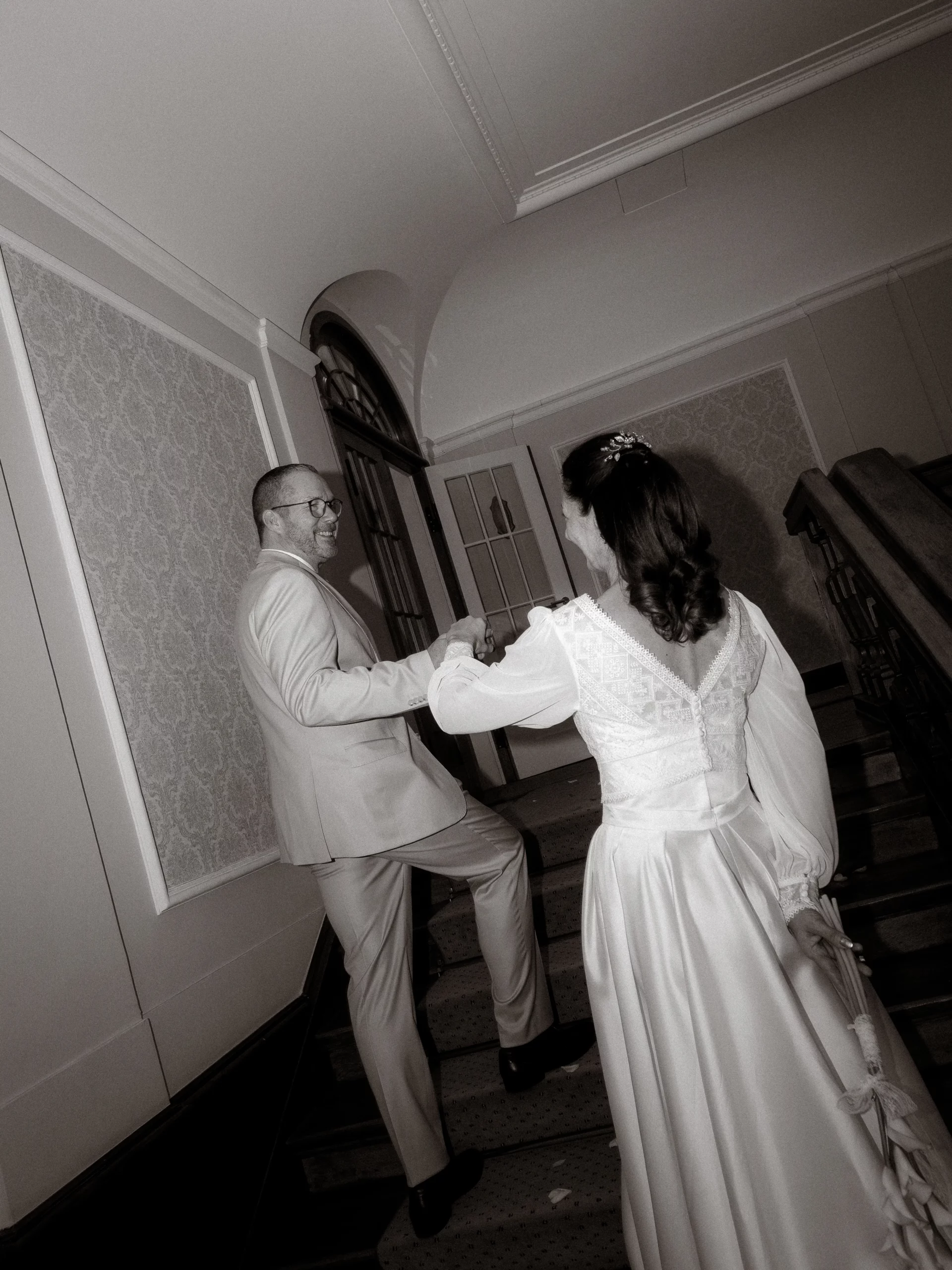 Hochzeitspaar steigt Treppe hinauf. Braut im Hochzeitskleid, Bräutigam im Anzug. Hochzeitsfotograf in [Stadt]