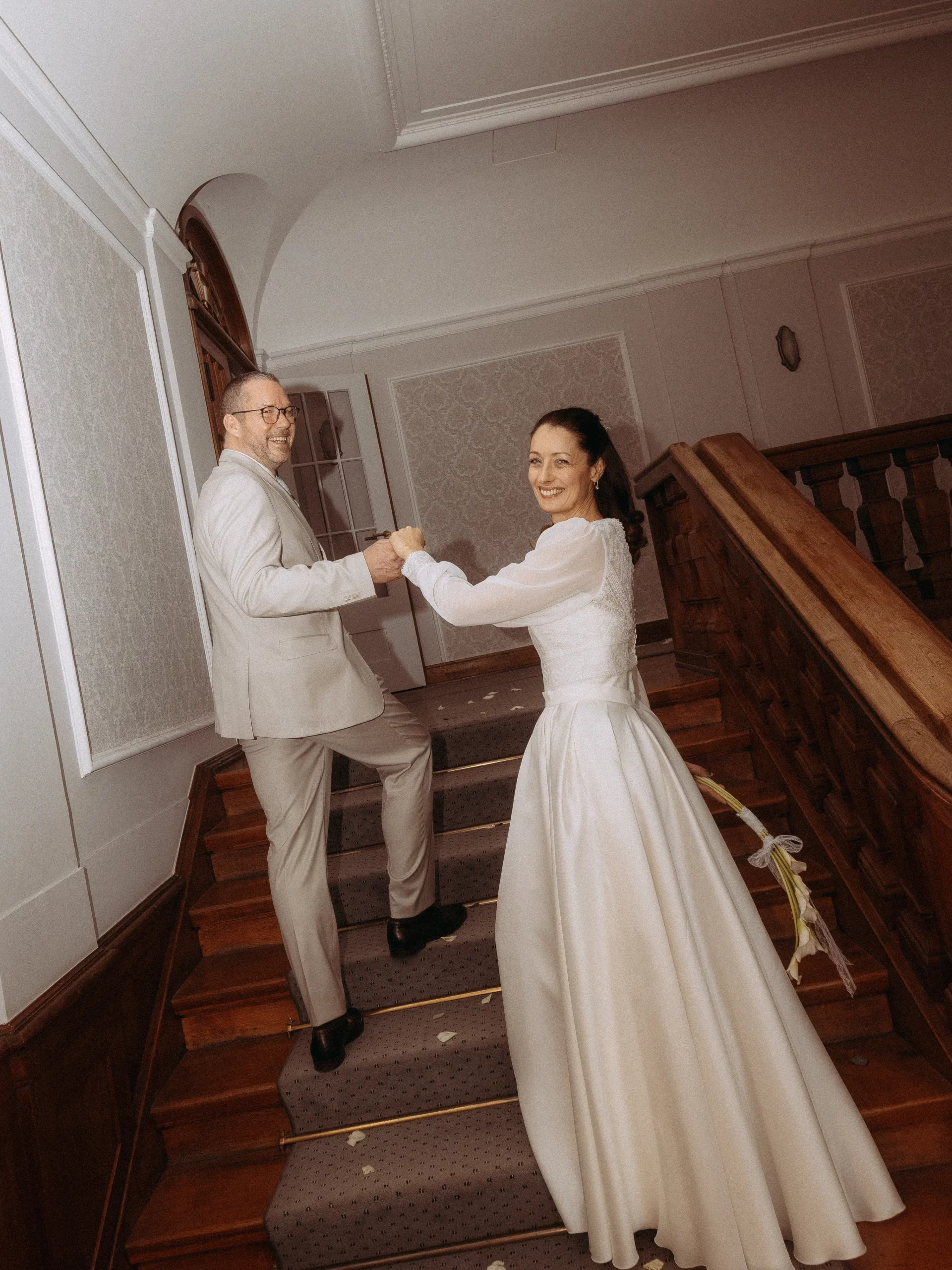 Brautpaar steigt Treppe hoch, hält Hände. Hochzeitsfotograf in [Stadt einfügen].