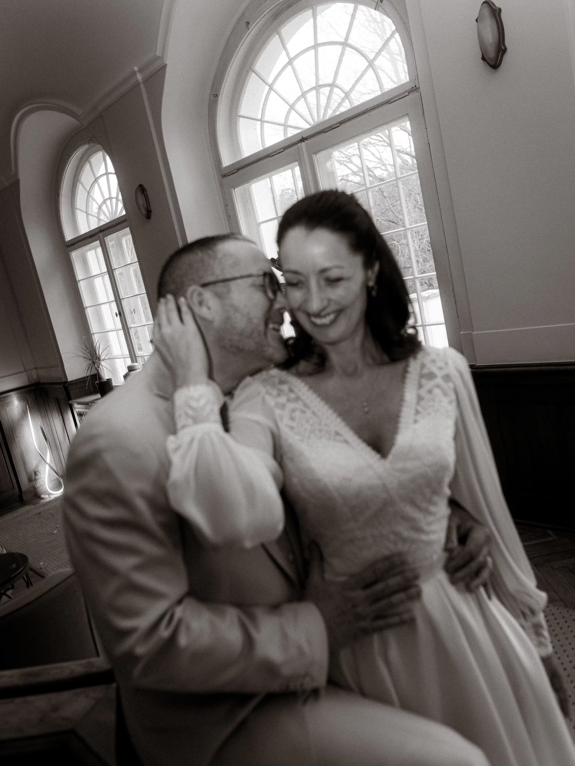 Brautpaar umarmt sich liebevoll vor Fenstern. Glückliche Hochzeit.