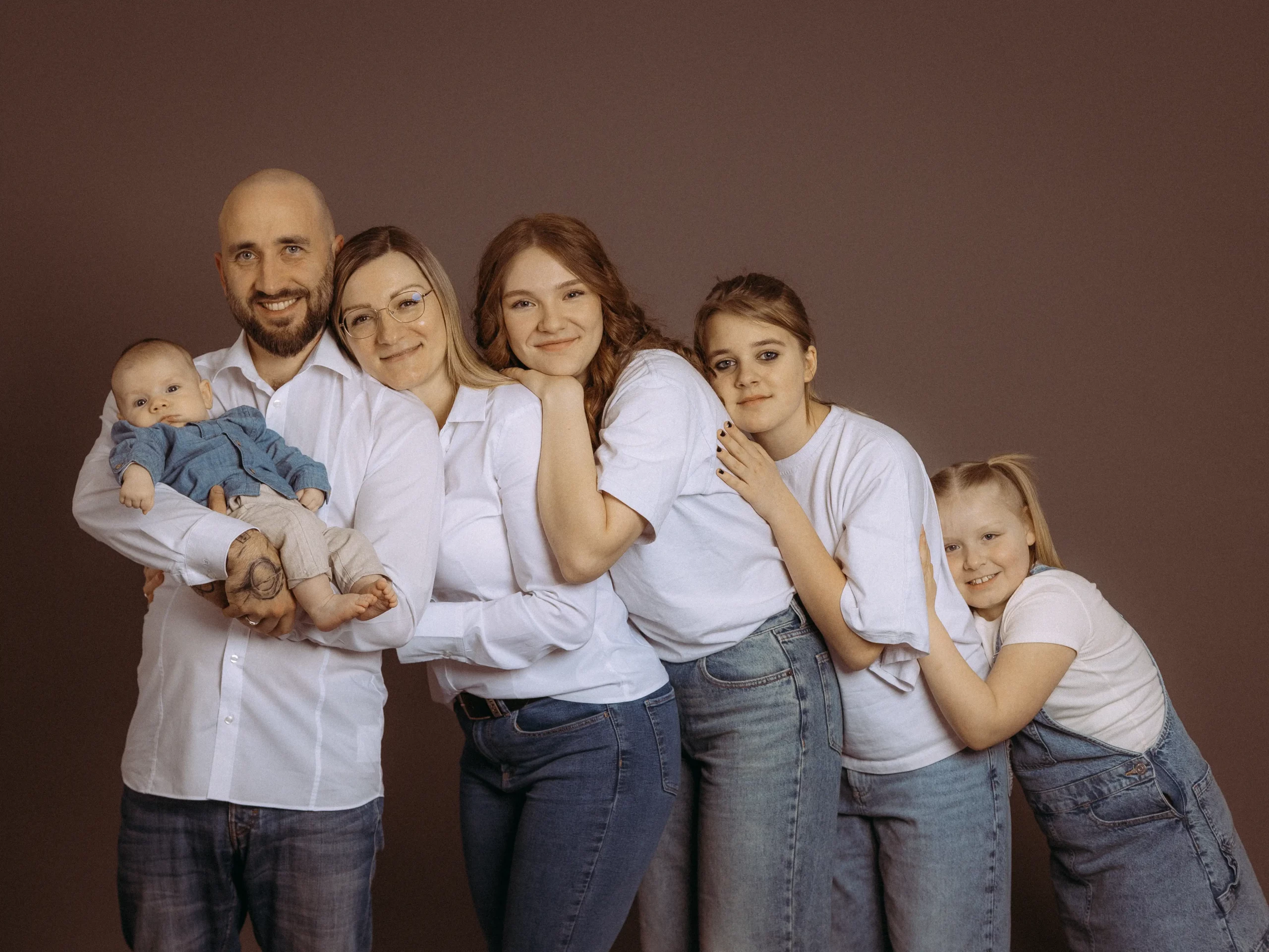 Eine glückliche Familie aus MV kuschelt sich aneinander. Der Vater hält ein Baby, während die Mutter und drei Töchter lächeln. Familienfotos MV mit dem Fotograf aus Schwerin.