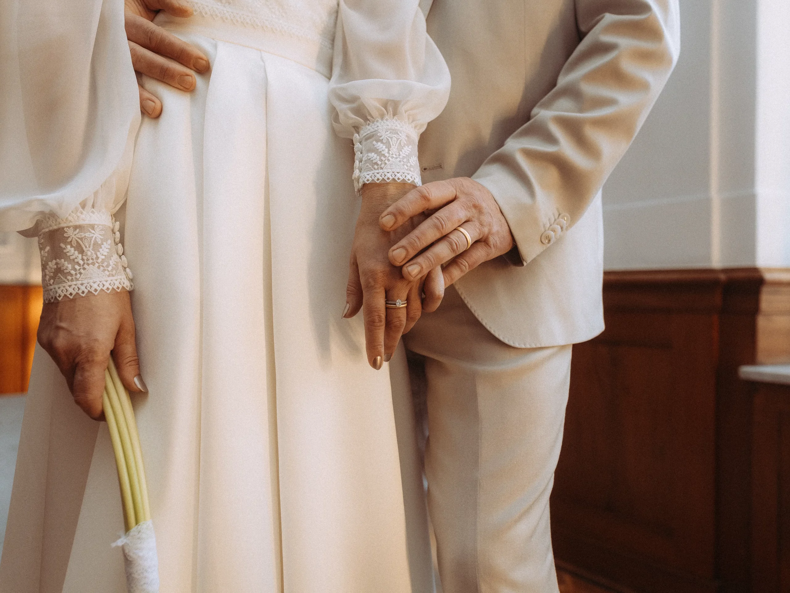 Brautpaar hält Hände, Eheringe sichtbar. Fokus auf die Verbundenheit bei der Hochzeit.