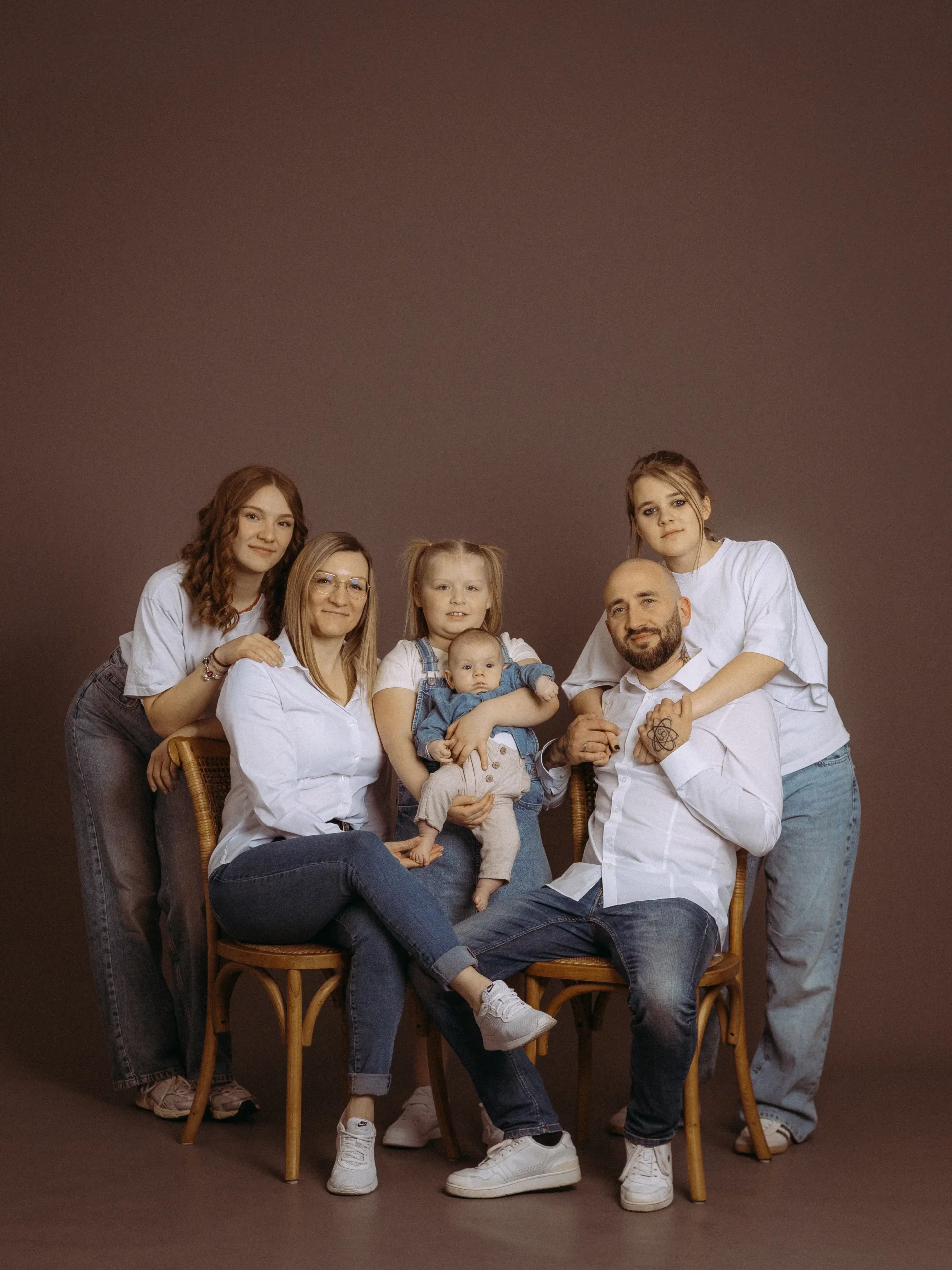 Eine glückliche Familie posiert für ein Familienfoto MV. Mutter, Vater, drei Töchter und ein Baby sitzen und stehen vor einem braunen Hintergrund. Der Fotograf in Schwerin hat die Familie gut in Szene gesetzt.