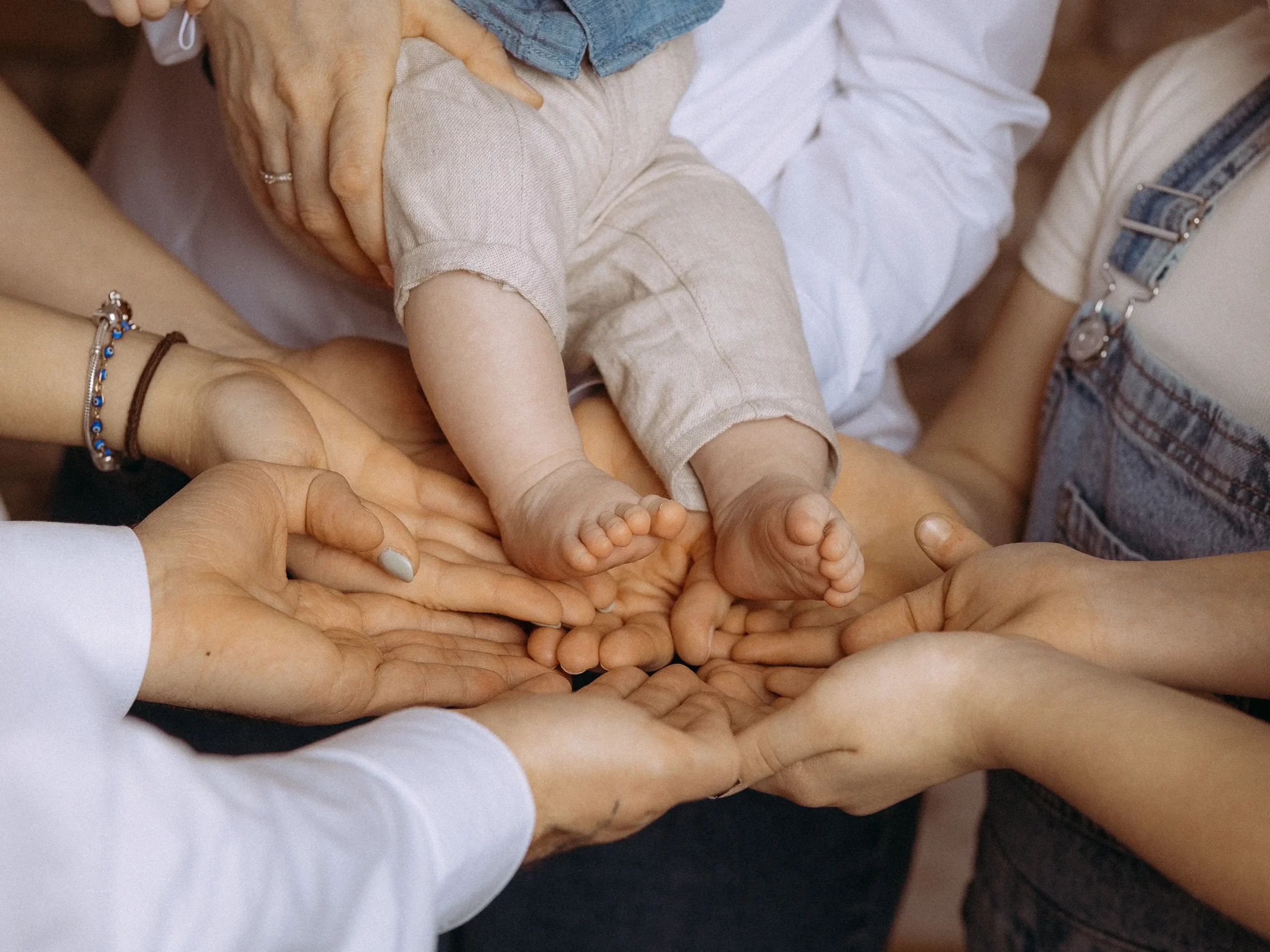 Mehrere Hände umarmen zärtlich die Füße eines Babys, gehalten von einer Person. Familienfotos MV zeigen Verbundenheit und Liebe. Fotograf in MV fängt emotionale Momente ein.