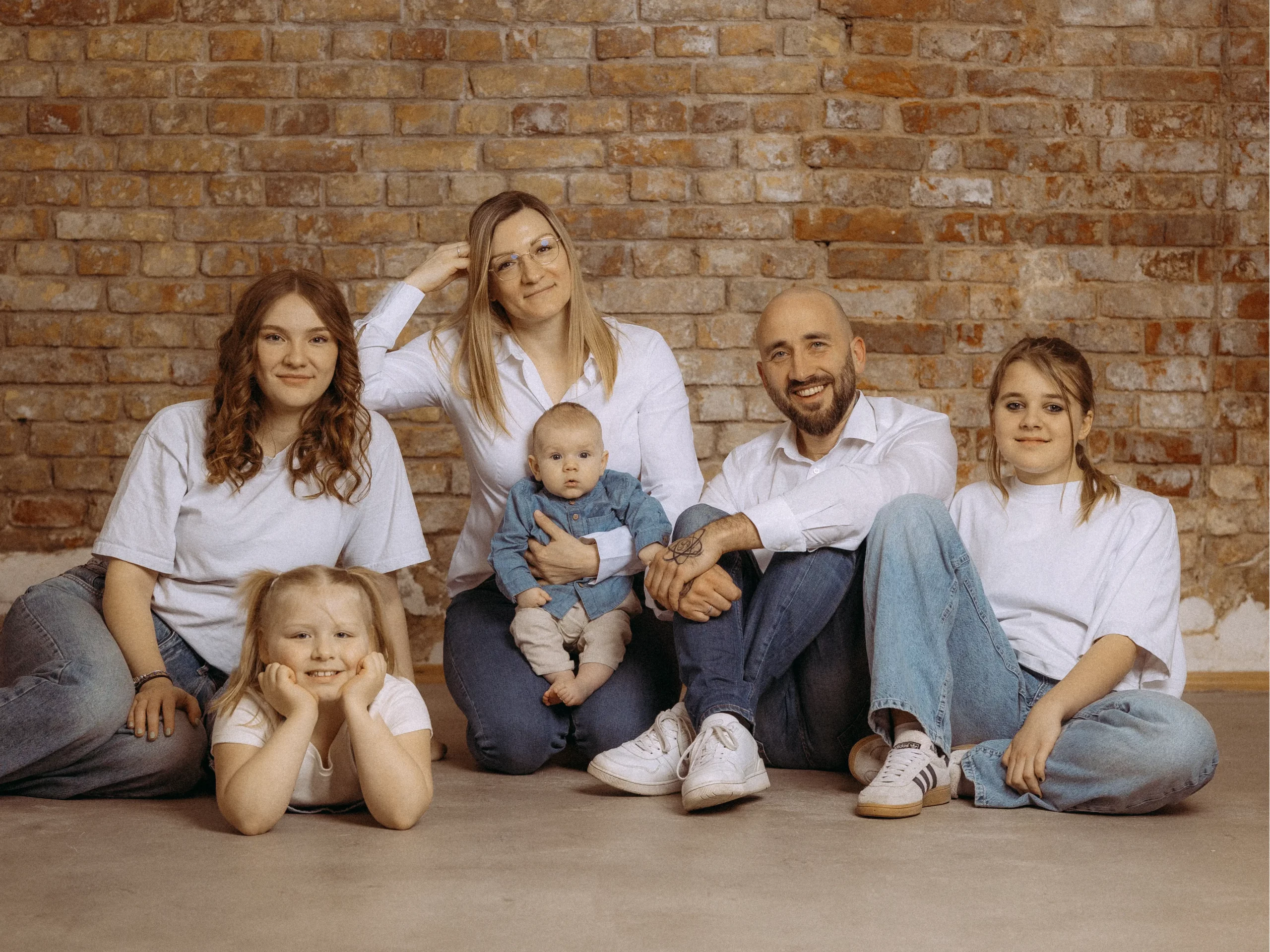 Eine glückliche Familie posiert vor einer Backsteinmauer. Die Eltern und ihre drei Töchter, darunter ein Baby, tragen lässige Kleidung. Familienfotos MV vom Fotograf in Schwerin.