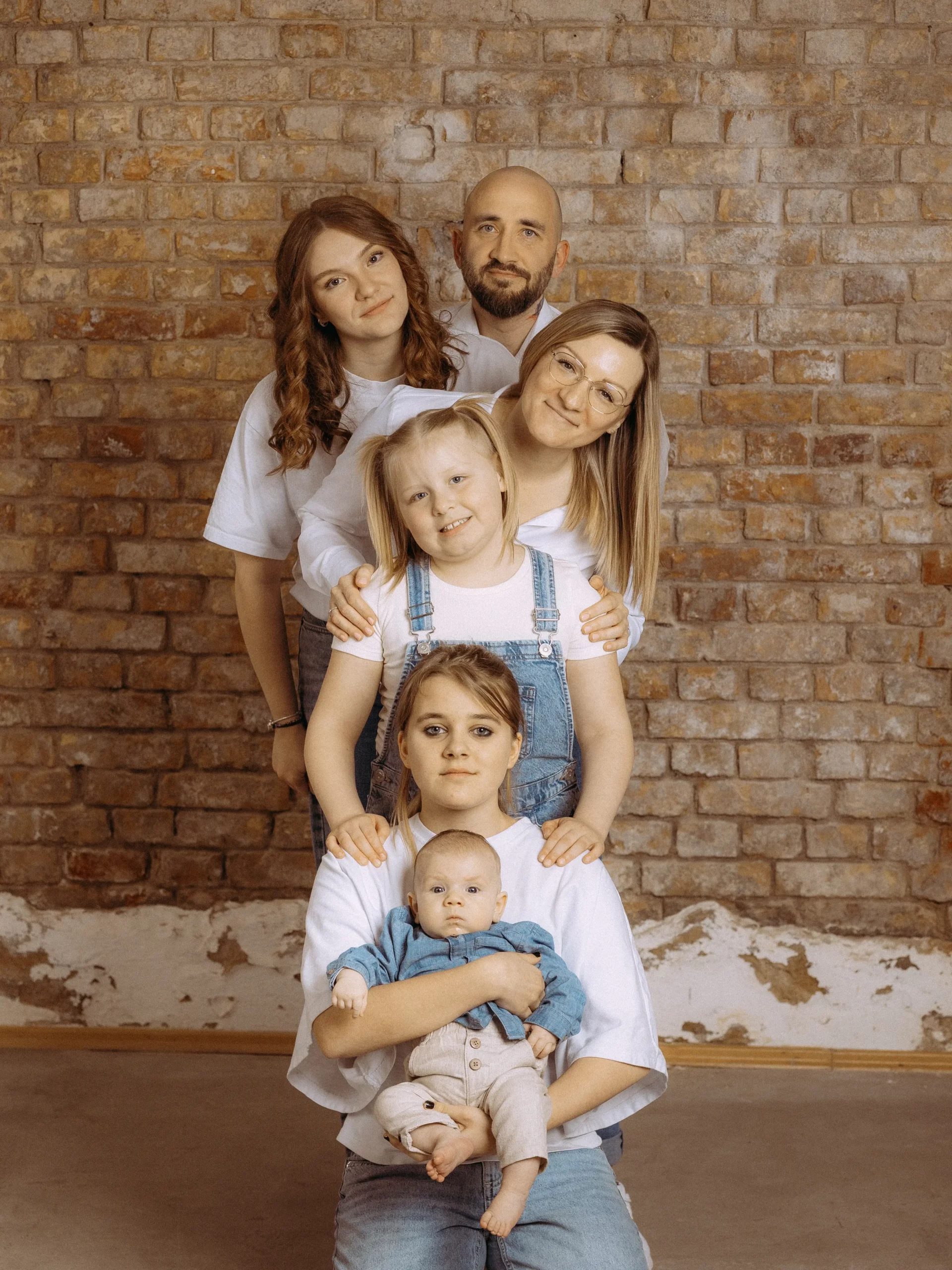 Eine Familie posiert vor einer Backsteinmauer. Die Mutter hält ein Baby, während ihre Töchter und der Vater dahinter stehen. Familienfotos MV.