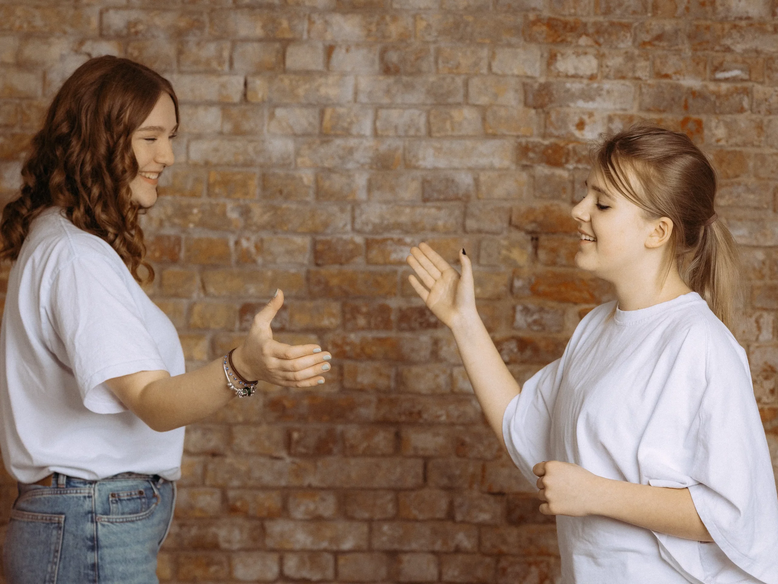 Zwei junge Frauen in weißen TShirts stehen vor einer Backsteinwand und scheinen sich High Five zu geben. Freundschaft und positive Stimmung. Fotograf in MV.