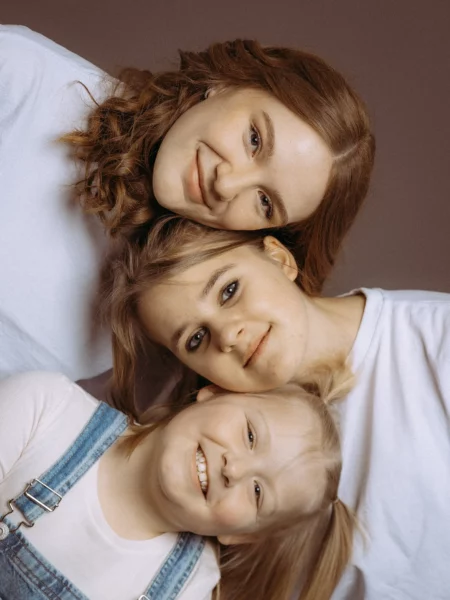 Drei lächelnde Schwestern liegen übereinander, die Älteste mit lockigem Haar. Familienfotos MV zeigen die Verbundenheit. Fotograf in MV hält diesen Moment fest.