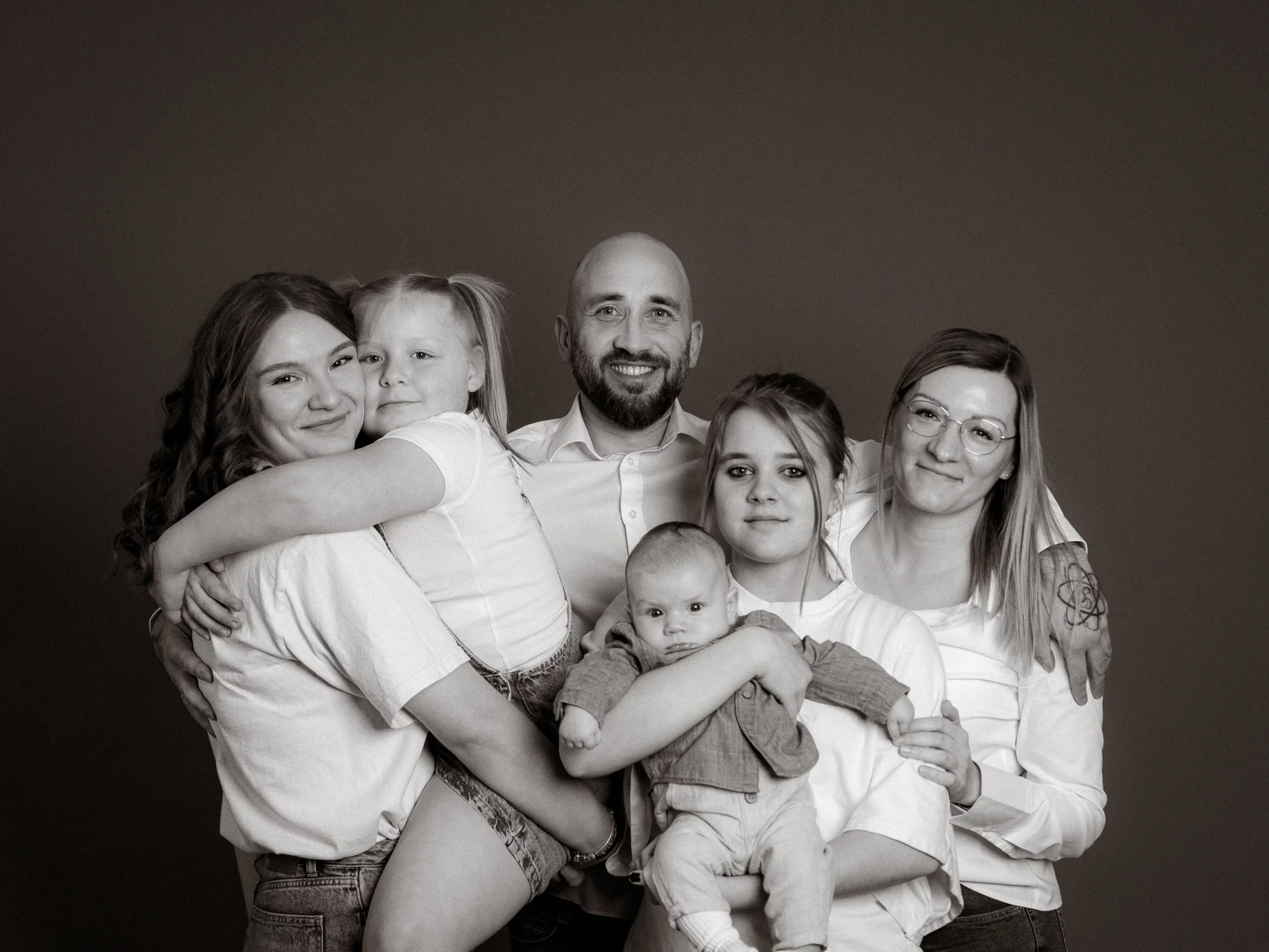 Familienfotos MV: Eine glückliche Familie posiert. Der Fotograf aus Schwerin hat ein Schwarzweißfoto von Eltern mit vier Kindern gemacht, die alle in hellen Oberteilen gekleidet sind.