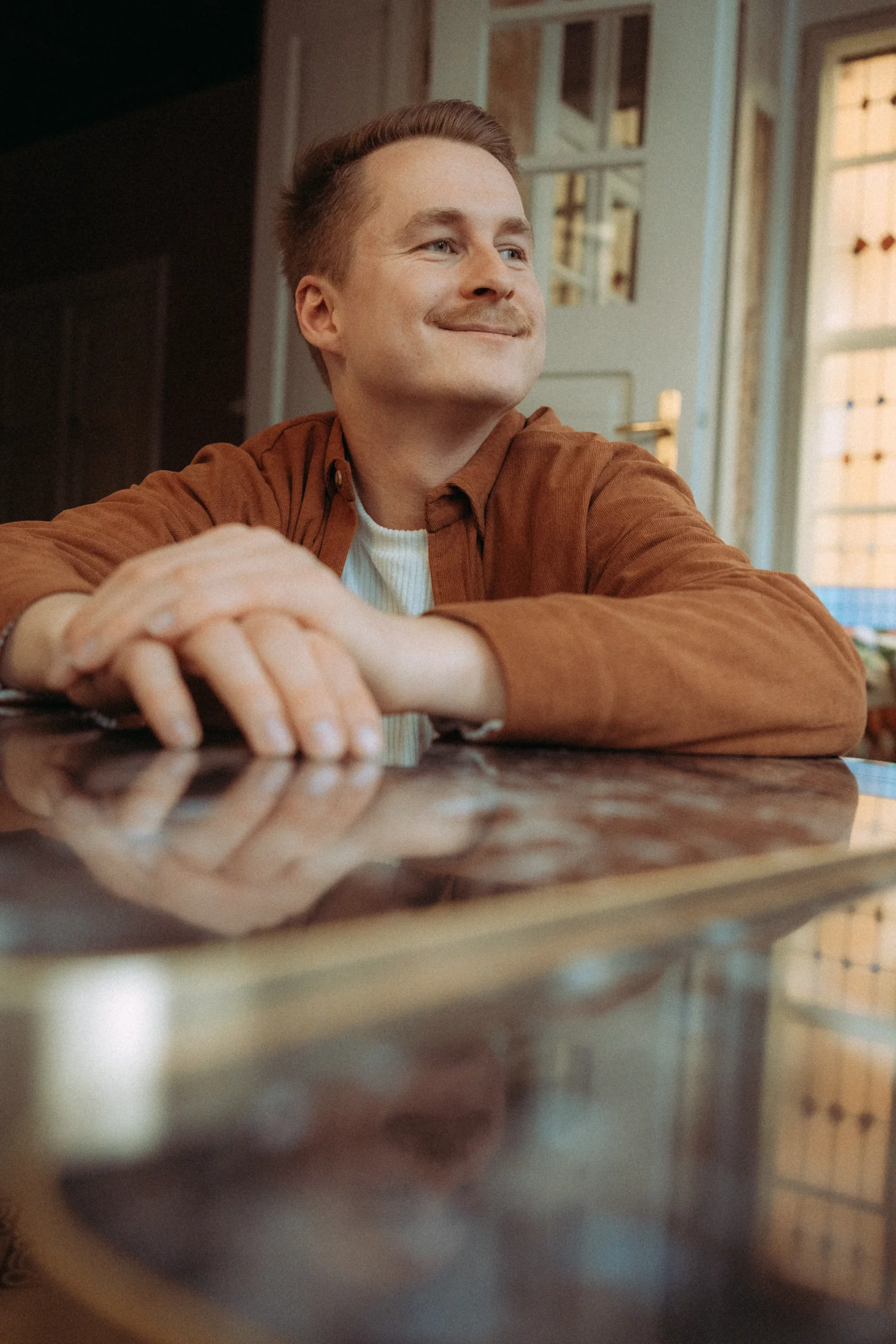 Mann lächelt am Tisch mit verschränkten Händen