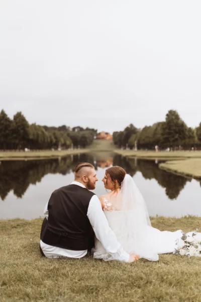 Brautpaar sitzt auf einer Wiese mit Blick auf einen See in Schwerin. Der Hochzeitsfotograf in Schwerin hat die beiden bei ihrer Hochzeit fotografiert.