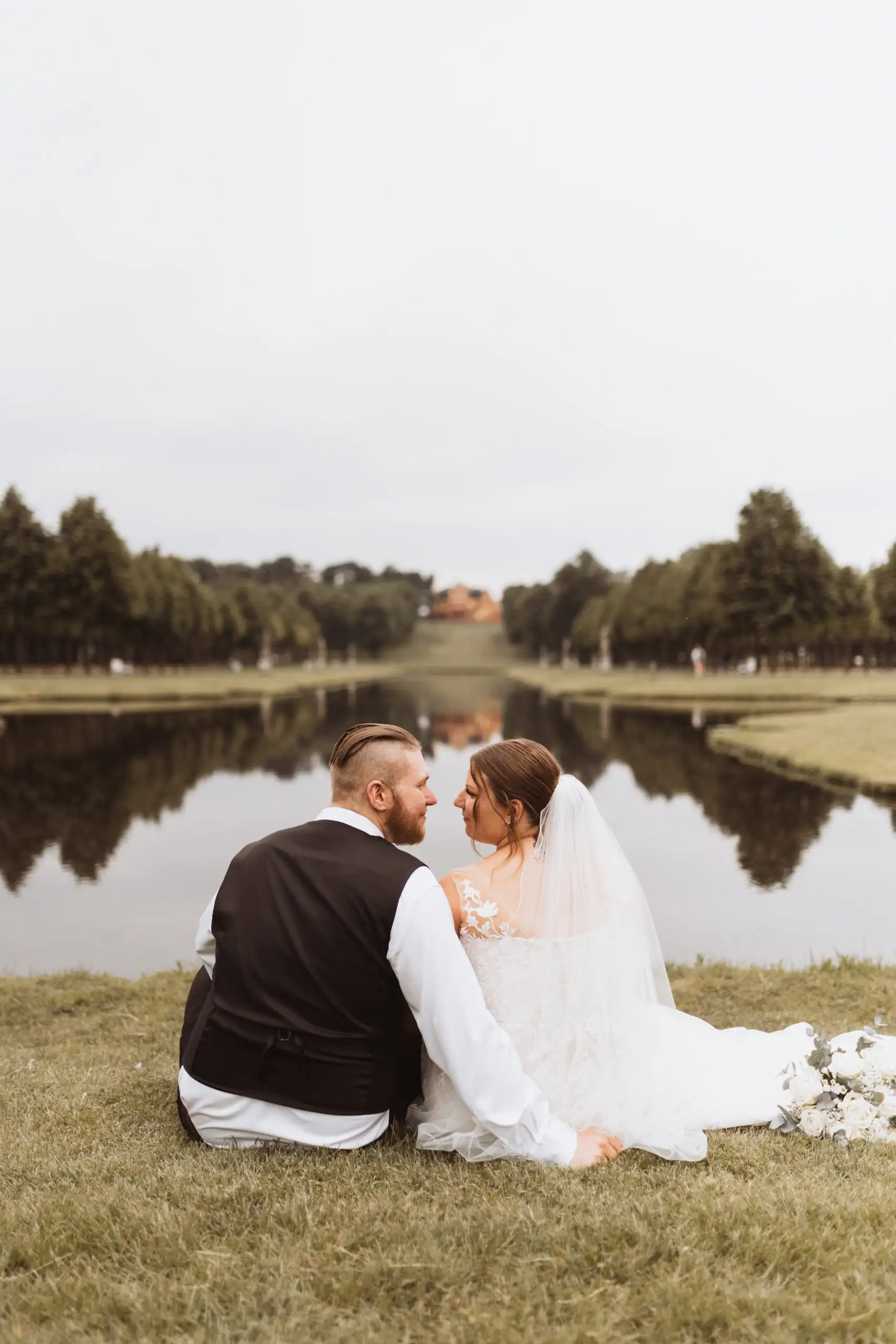 Brautpaar sitzt auf einer Wiese mit Blick auf einen See in Schwerin. Der Hochzeitsfotograf in Schwerin hat die beiden bei ihrer Hochzeit fotografiert.