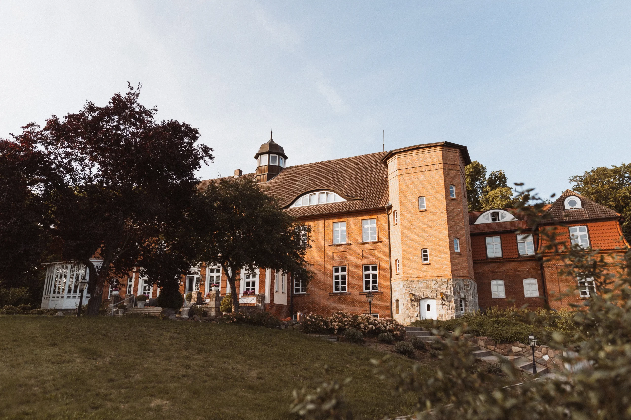 Historisches Backsteingebäude mit Turm, umgeben von Grünflächen und Bäumen. Architekturdetail mit roten Ziegeln und weißen Fenstern. Einladende Szene für Fotograf in MV oder Familienfotos MV.