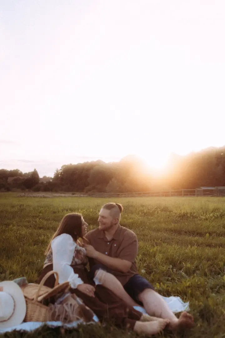 Ein glückliches Paar sitzt während einer romantischen Golden Hour auf einer Wiese, umgeben von warmem Sonnenlicht und einer malerischen Naturkulisse. Die beiden genießen einen entspannten Moment bei einem Picknick für professionelle Pärchenfotos Schwerin.