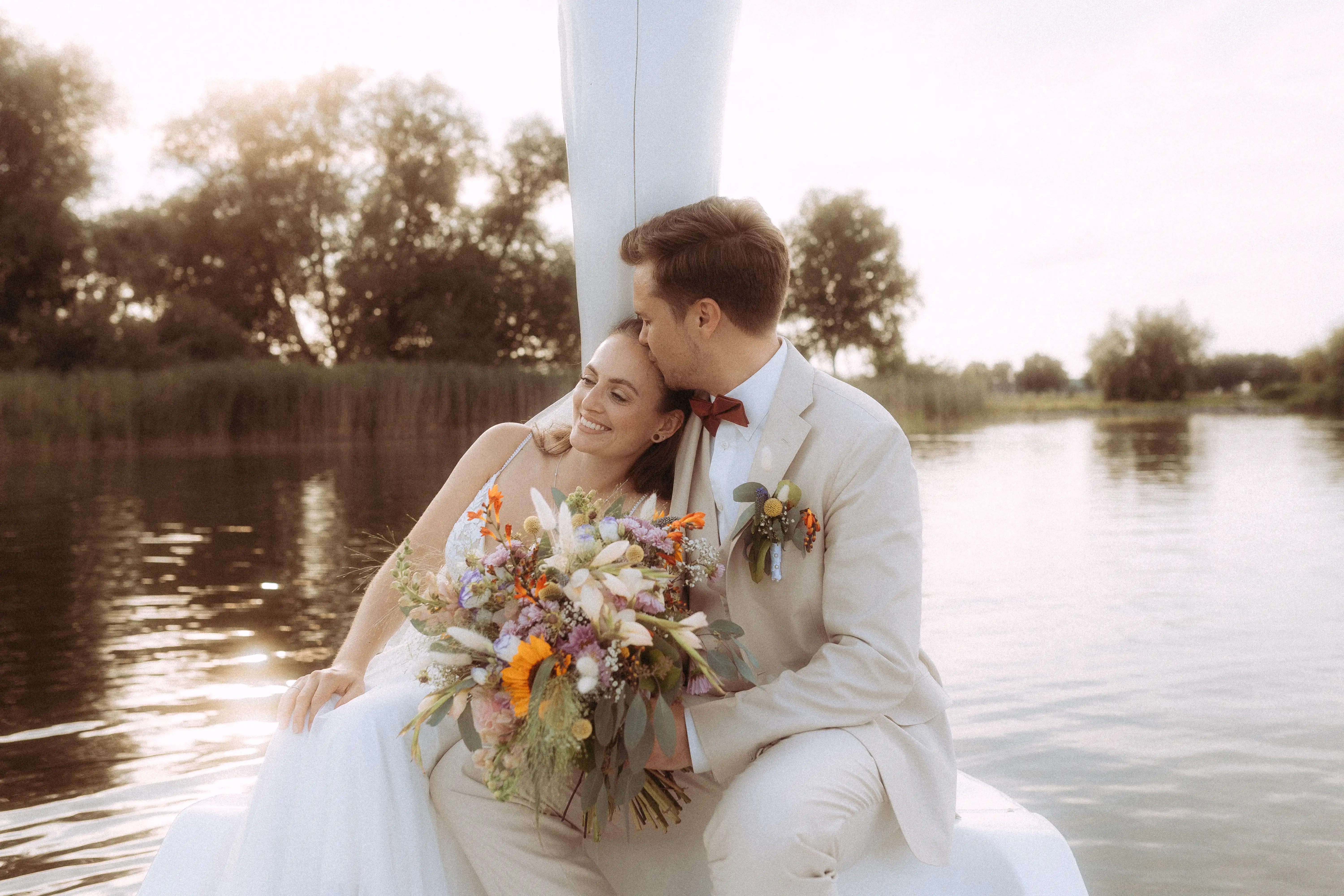 Hochzeitsfotograf in Schwerin: Ein frisch vermähltes Paar auf einem Boot, der Bräutigam küsst die Braut auf die Stirn, sie hält einen Blumenstrauß. Hochzeitsfotograf in Schwerin: Ein frisch vermähltes Paar auf einem Boot, der Bräutigam küsst die Braut auf die Stirn, sie hält einen Blumenstrauß.