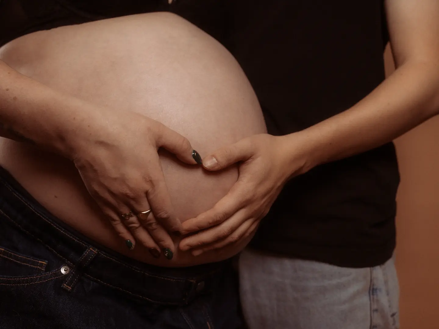 Ein Paar formt mit den Händen ein Herz auf dem nackten Babybauch einer schwangeren Frau, eine intime Momentaufnahme für professionelle Familienfotos in Schwerin.