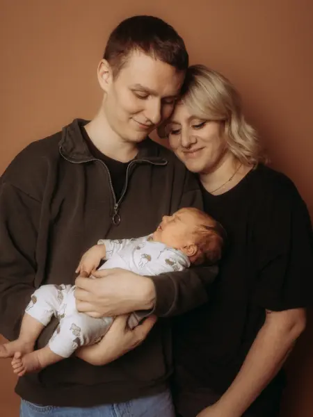 Ein junges Paar hält liebevoll sein neugeborenes Baby in den Armen, während beide Elternteile sanft auf das schlafende Kind herabblicken. Die Aufnahme entstand in einem Fotostudio in Schwerin und fängt einen intimen Moment als Familienfotograf in Schwerin ein.