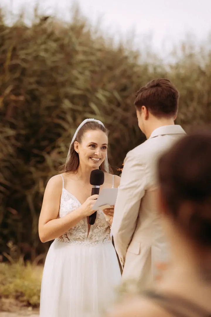 Eine strahlende Braut in einem weißen Spitzenkleid liest während der Trauung ihr Eheversprechen von einer Karte vor, während sie liebevoll ihren Bräutigam ansieht – festgehalten von einem Hochzeitsfotograf in Schwerin und MV.