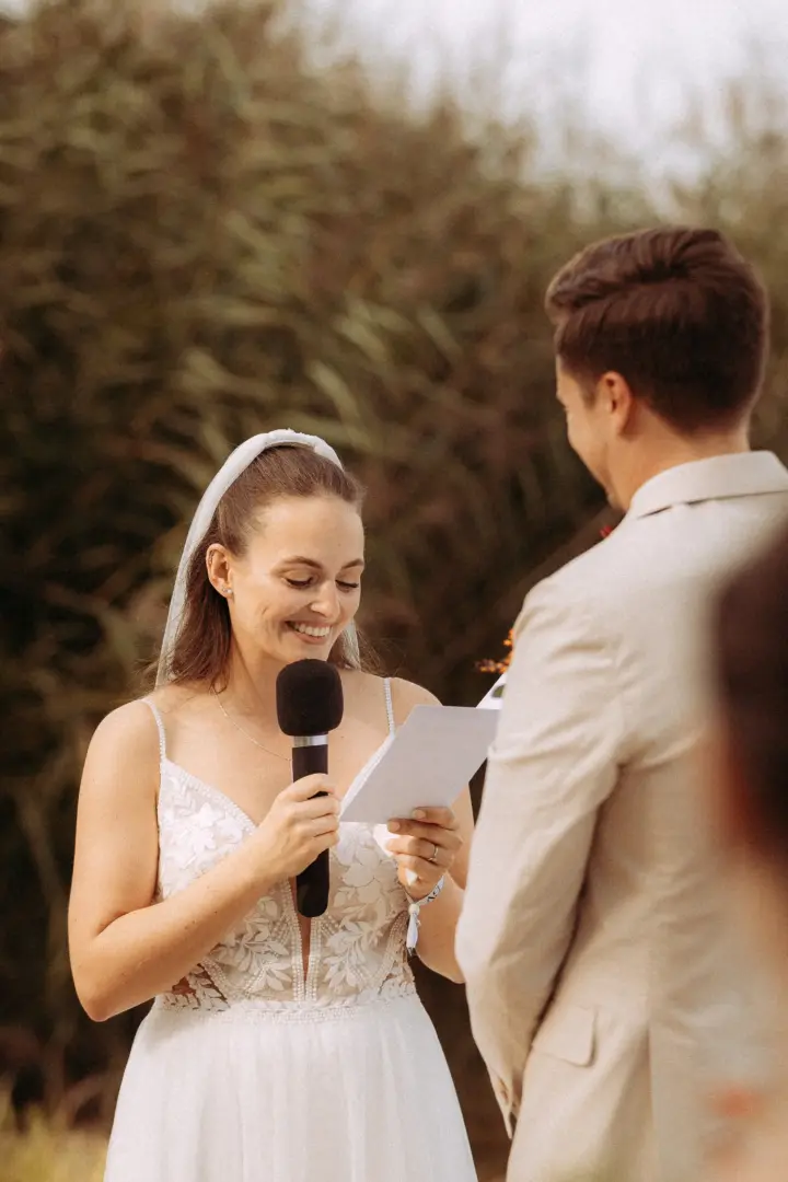 Eine strahlende Braut liest während der Trauung im Freien ihre Eheversprechen vor, während der Bräutigam sie liebevoll ansieht. Die emotionale Szene wurde von einem Hochzeitsfotograf in Schwerin und MV in einem natürlichen, warmen Stil festgehalten.