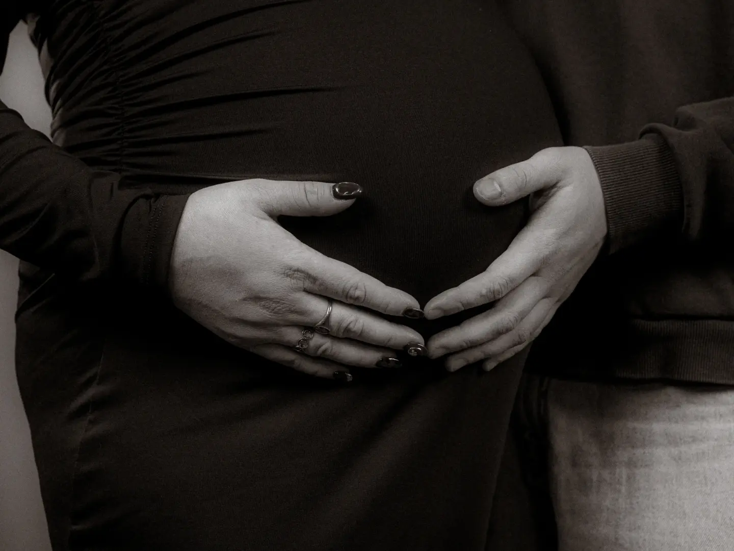Nahaufnahme eines schwangeren Bauches, der liebevoll von den Händen einer Frau mit Ringen und einem Partner umschlossen wird. Das emotionale Bild in Schwarz-Weiß fängt eine intime Schwangerschaftserinnerung ein, ideal für ein professionelles Fotoshooting beim Fotograf für Familien in Schwerin.