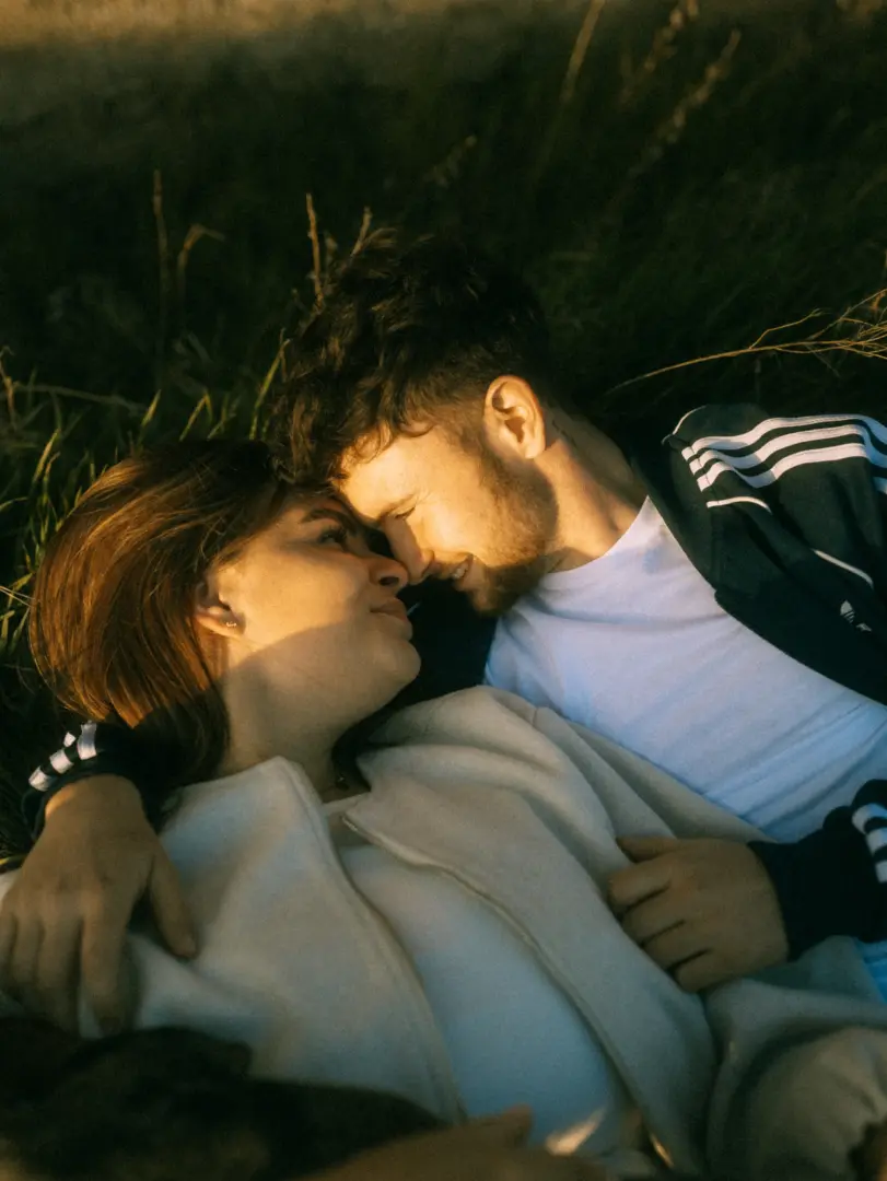 Ein junges Paar liegt sich in einer romantischen Lovestory in Schwerin und MV liebevoll gegenüber im Gras. Das warme Licht der untergehenden Sonne taucht die Szene in goldene Töne, während sie sich eng verbunden in die Augen schauen und eine intime, emotionale Stimmung genießen.