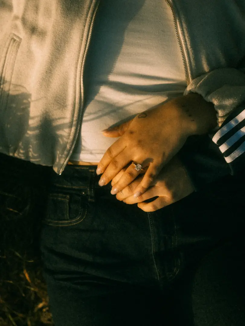 Nahaufnahme eines Paares, das sich liebevoll an den Händen hält, wobei der Fokus auf einem eleganten Verlobungsring an der Hand der Frau liegt. Diese intimen Pärchenfotos in Schwerin fangen die romantische Stimmung in warmem Abendlicht perfekt ein.