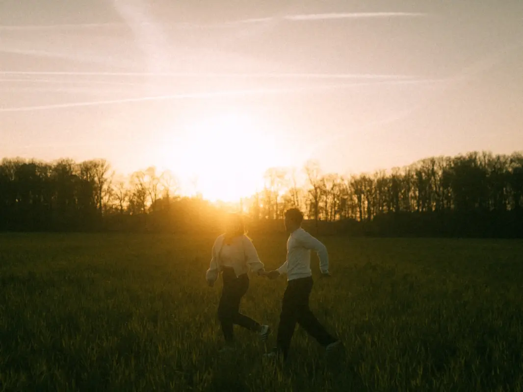 Ein junges Paar hält händchenhaltend bei einem romantischen Spaziergang durch ein goldenes Feld im warmen Licht des Sonnenuntergangs inne. Die stimmungsvolle Atmosphäre unterstreicht ihre Verbundenheit bei einem Shooting für Pärchenfotos in Schwerin.