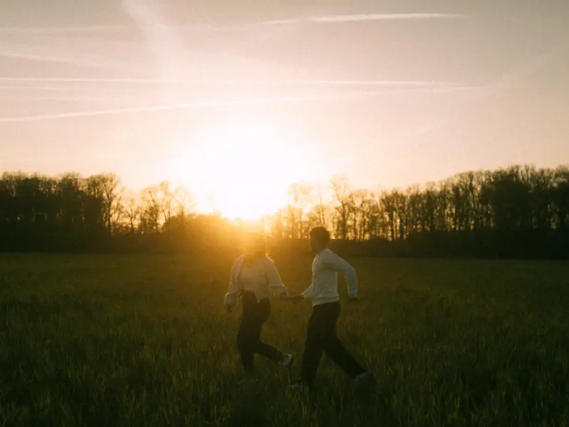 Ein junges Paar hält händchenhaltend bei einem romantischen Spaziergang durch ein goldenes Feld im warmen Licht des Sonnenuntergangs inne. Die stimmungsvolle Atmosphäre unterstreicht ihre Verbundenheit bei einem Shooting für Pärchenfotos in Schwerin.