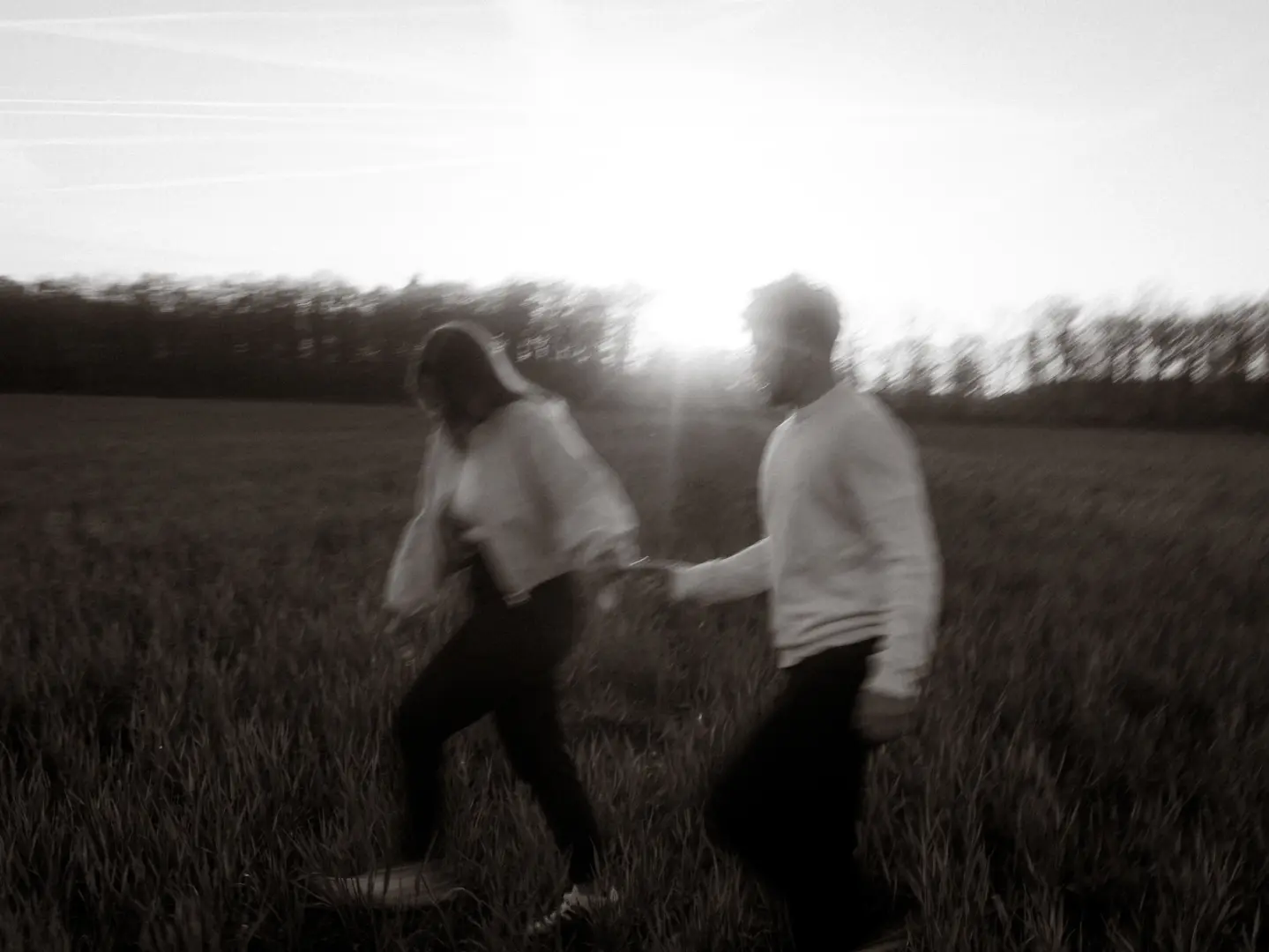 Ein Paar bei einem romantischen Spaziergang in einem Feld bei Sonnenuntergang. Die bewegungsunscharfe Aufnahme fängt einen intimen Moment ein, während die beiden sich an den Händen halten. Ästhetische Pärchenfotos Schwerin in natürlicher Lichtstimmung.