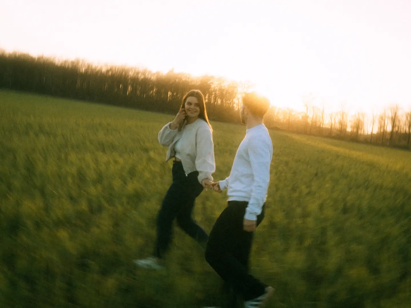 Ein glückliches Paar spaziert bei goldenem Sonnenuntergang händchenhaltend durch ein grünes Feld. Die romantische Stimmung wird durch den weichen Lichtschein und die natürliche Umgebung unterstrichen. Eine wunderschöne Aufnahme für Pärchenfotos in Schwerin.